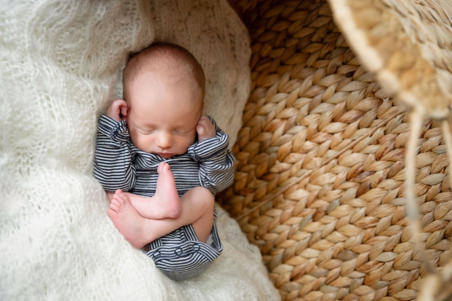 A small baby lies on a woven natural fiber rug while wearing a striped outfit.