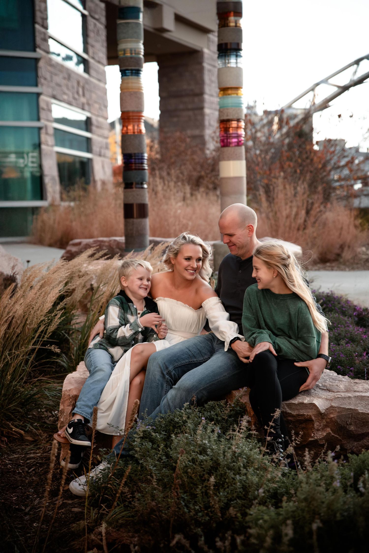 Family sitting together on stone steps surrounded by ornamental grasses in an urban setting.