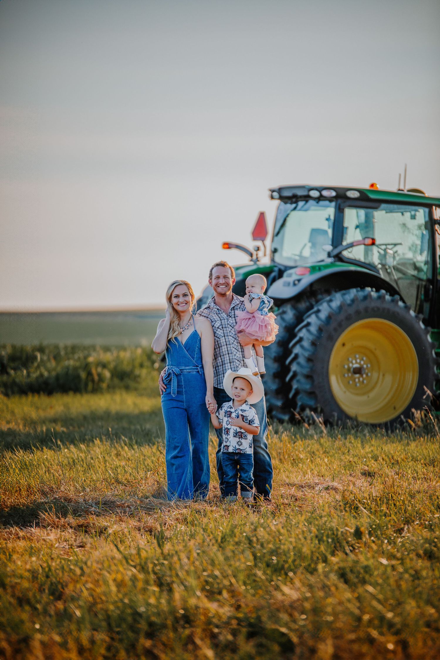 Family posing together in a golden field with large tractors in the background.