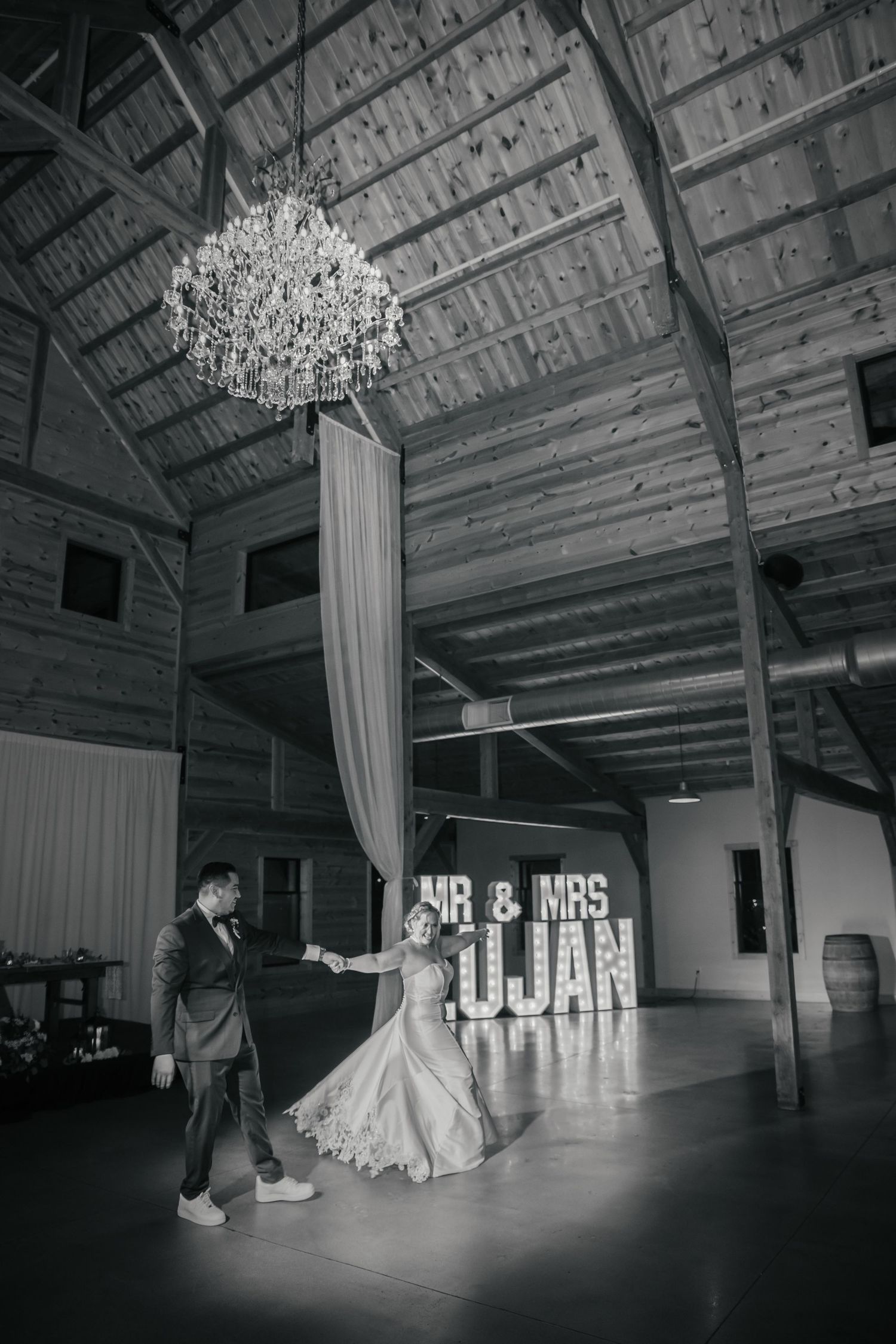 Black and white reception venue photo showing illuminated Mr & Mrs sign and chandelier.
