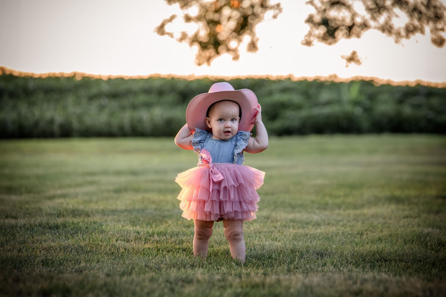 Child in pink tutu twirls through a green field at sunset.