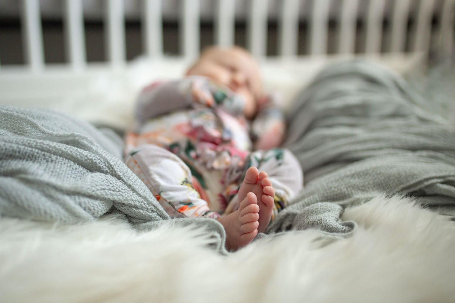 Close-up of sleeping baby on gray blanket in crib.