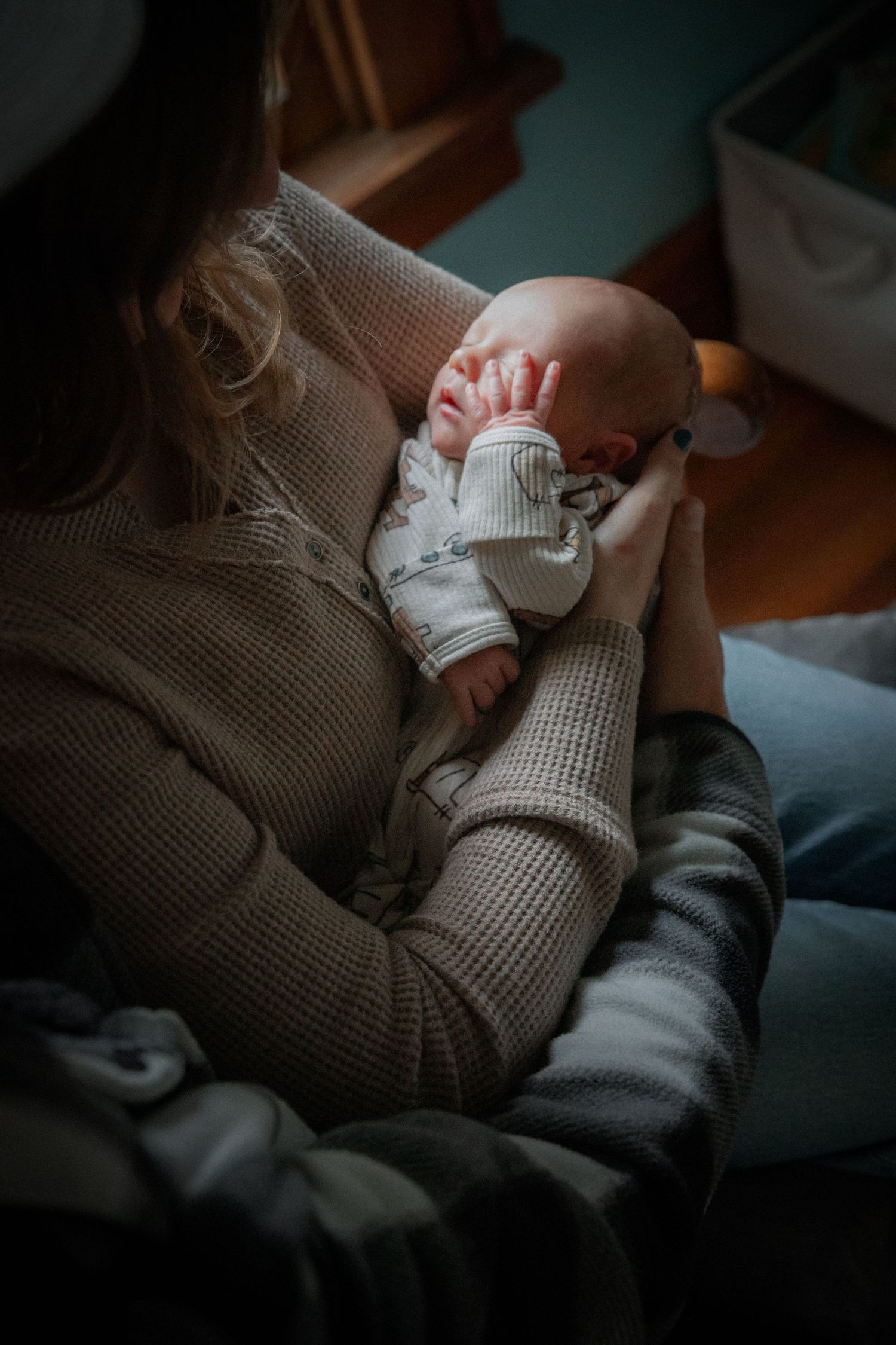 Close-up view of hands holding a newborn baby wrapped in a white blanket against a gray textured blanket background.
