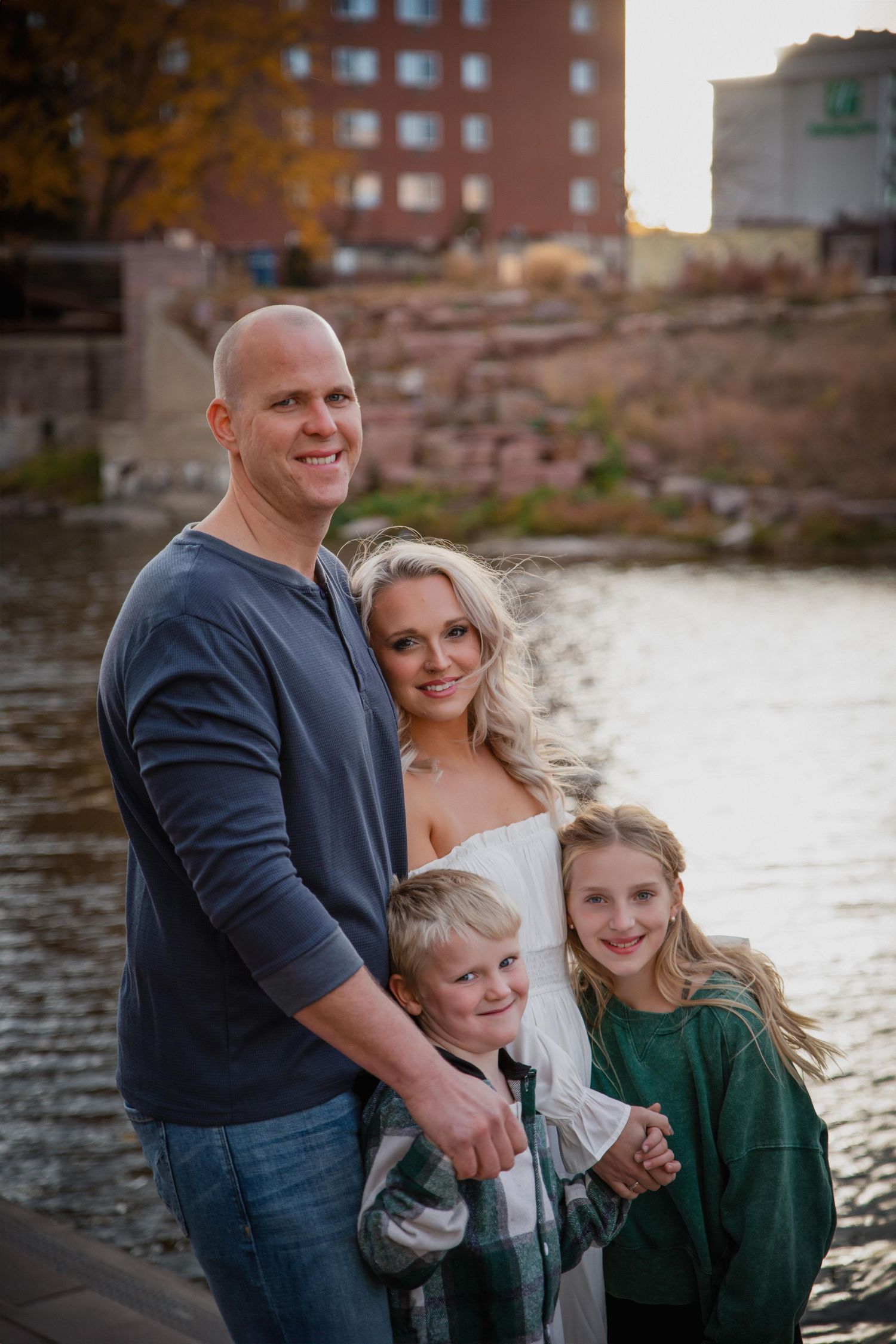 Family of four poses together by a waterfront during golden hour.