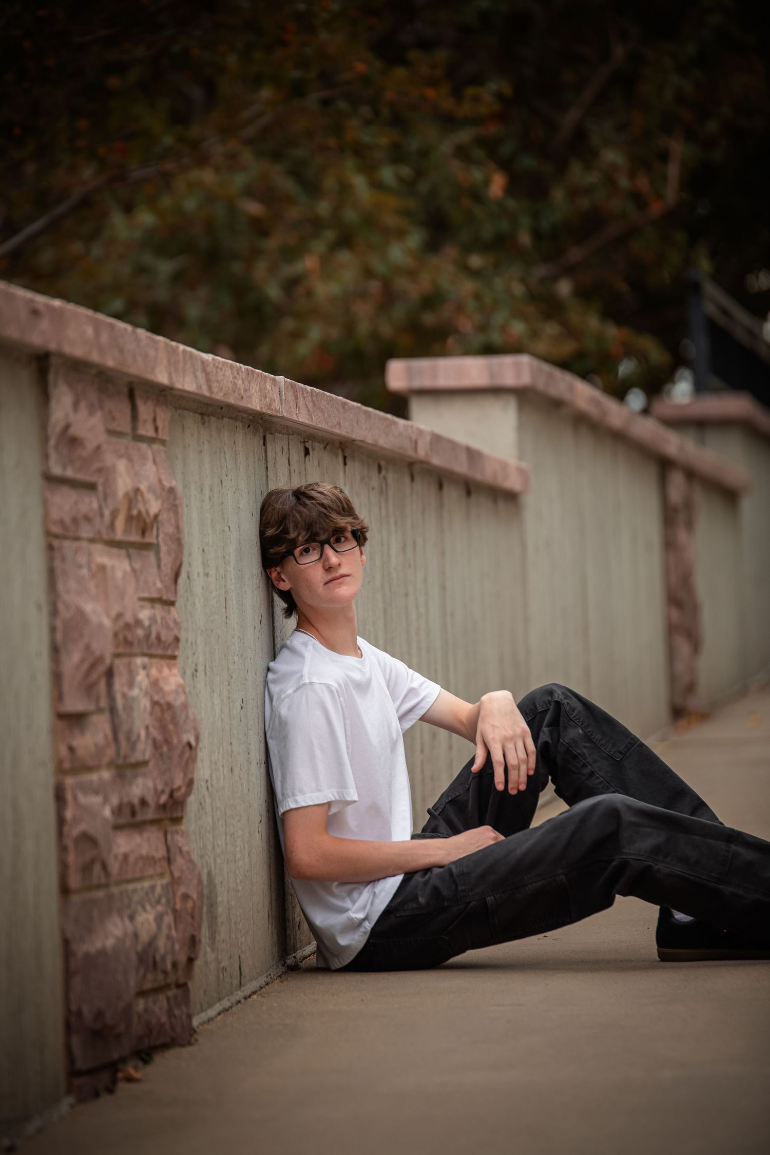 A person in a white t-shirt and dark pants reclines against a stone wall in an artistic outdoor portrait series.