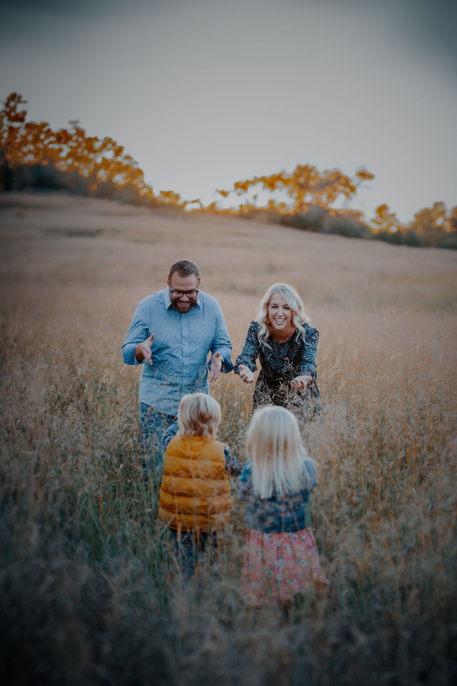 A family walks together through a golden autumn field at sunset casting long shadows among the tall grass.
