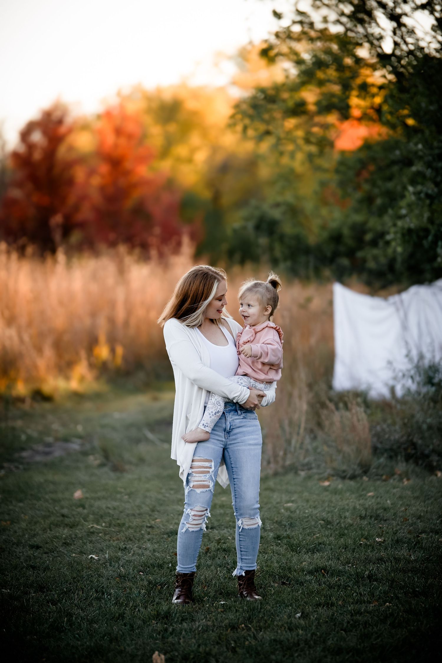 Candid outdoor portrait in autumn field at golden hour with person in distressed jeans holding small child. Photographer in Sioux Falls, SD