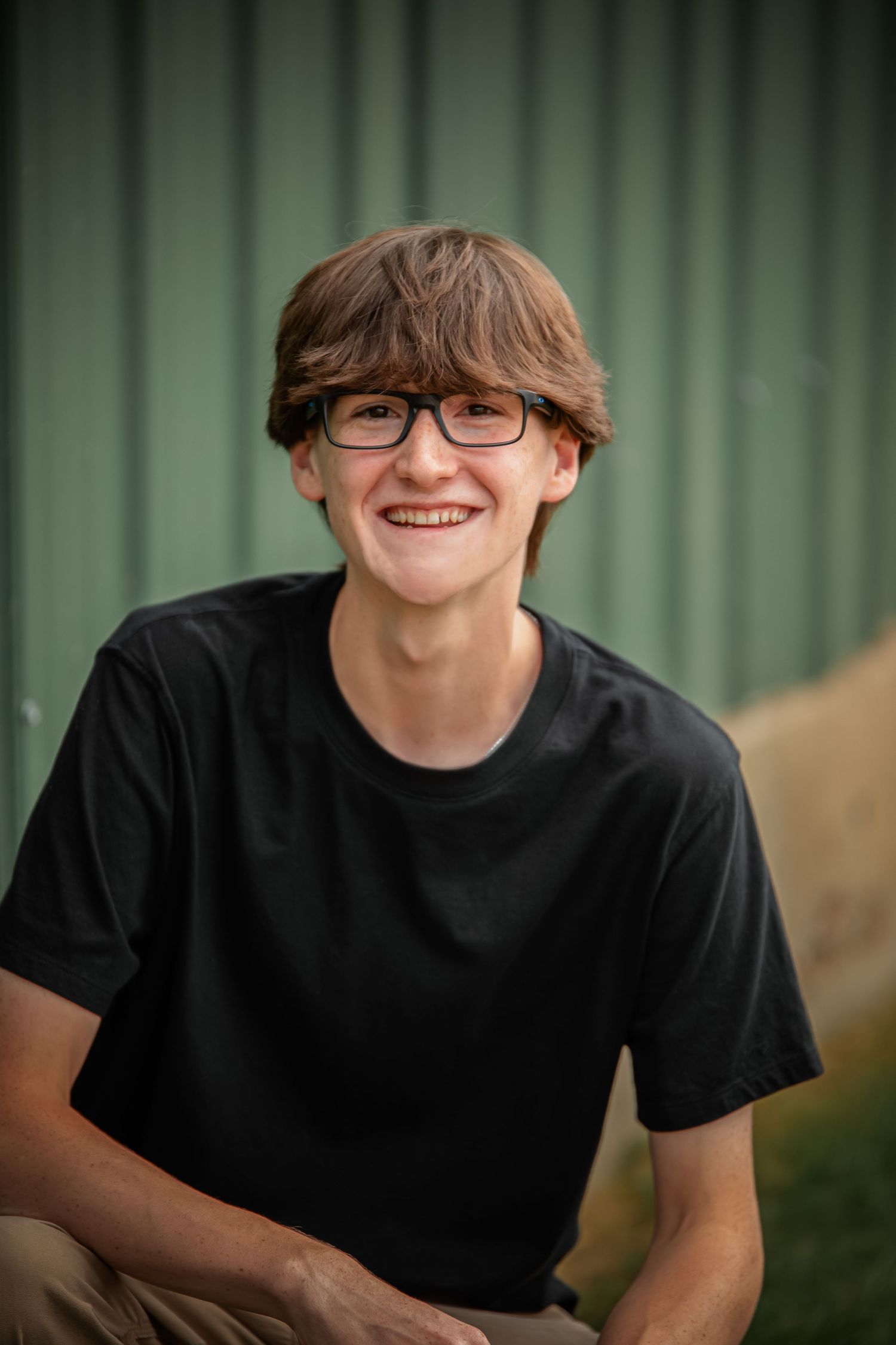 Portrait of student wearing glasses and black t-shirt against green background. Photographer in Sioux Falls, SD