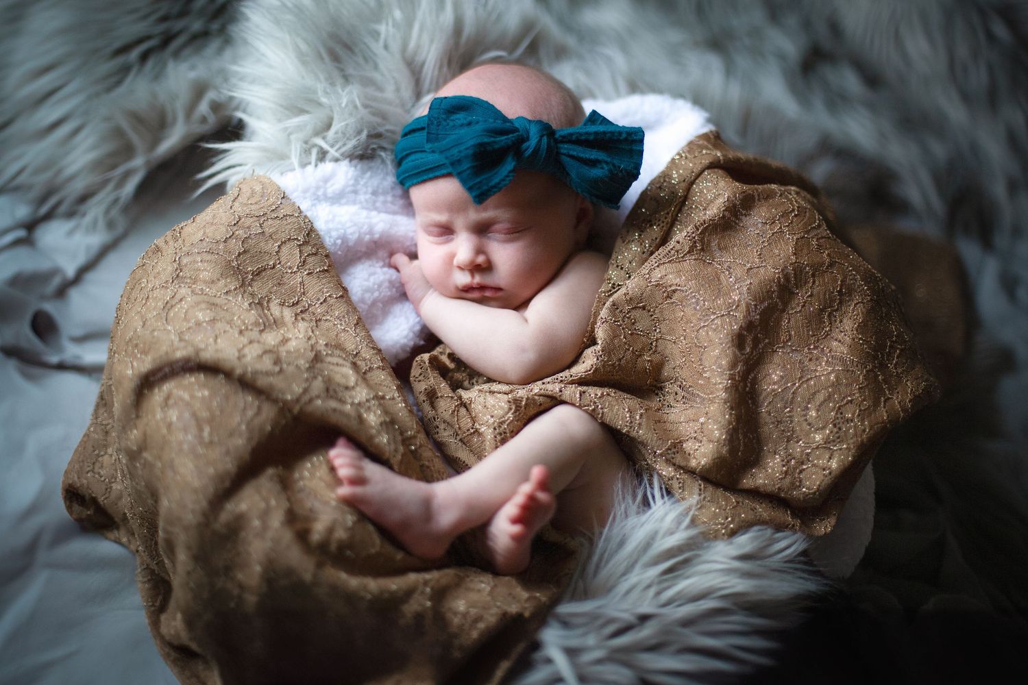 Sleeping infant wrapped in brown blanket on soft grey fur backdrop. Photographer in Sioux Falls, SD