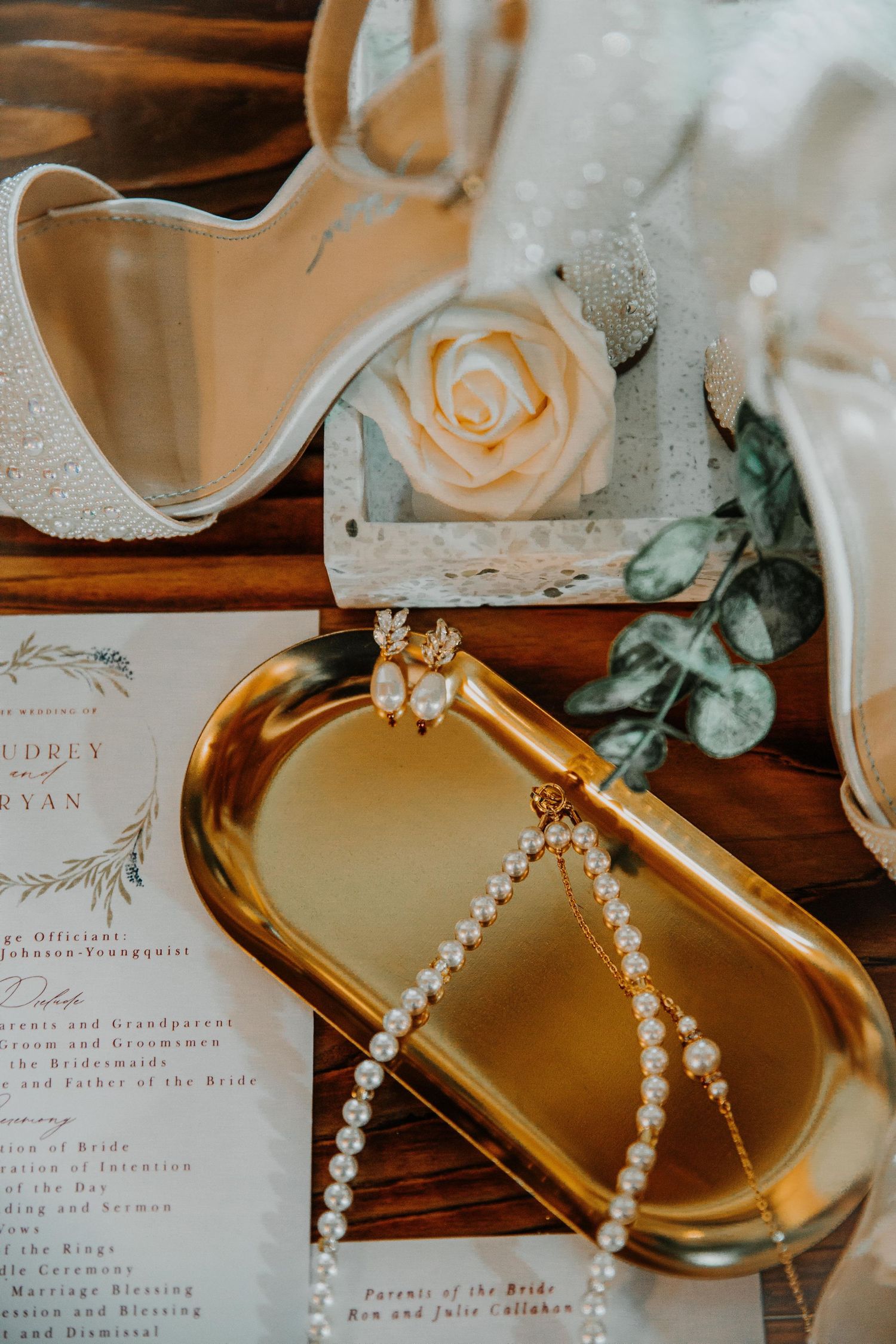 Wedding invitation suite with pearl jewelry and blush roses on metallic gold tray.