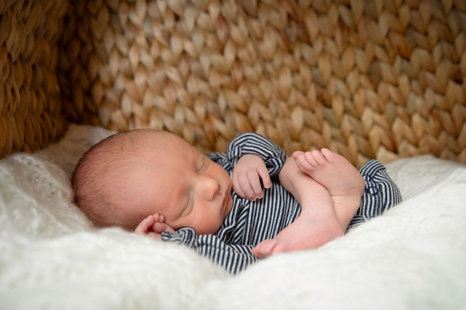 Sleeping infant in striped onesie rests peacefully on soft white blanket.