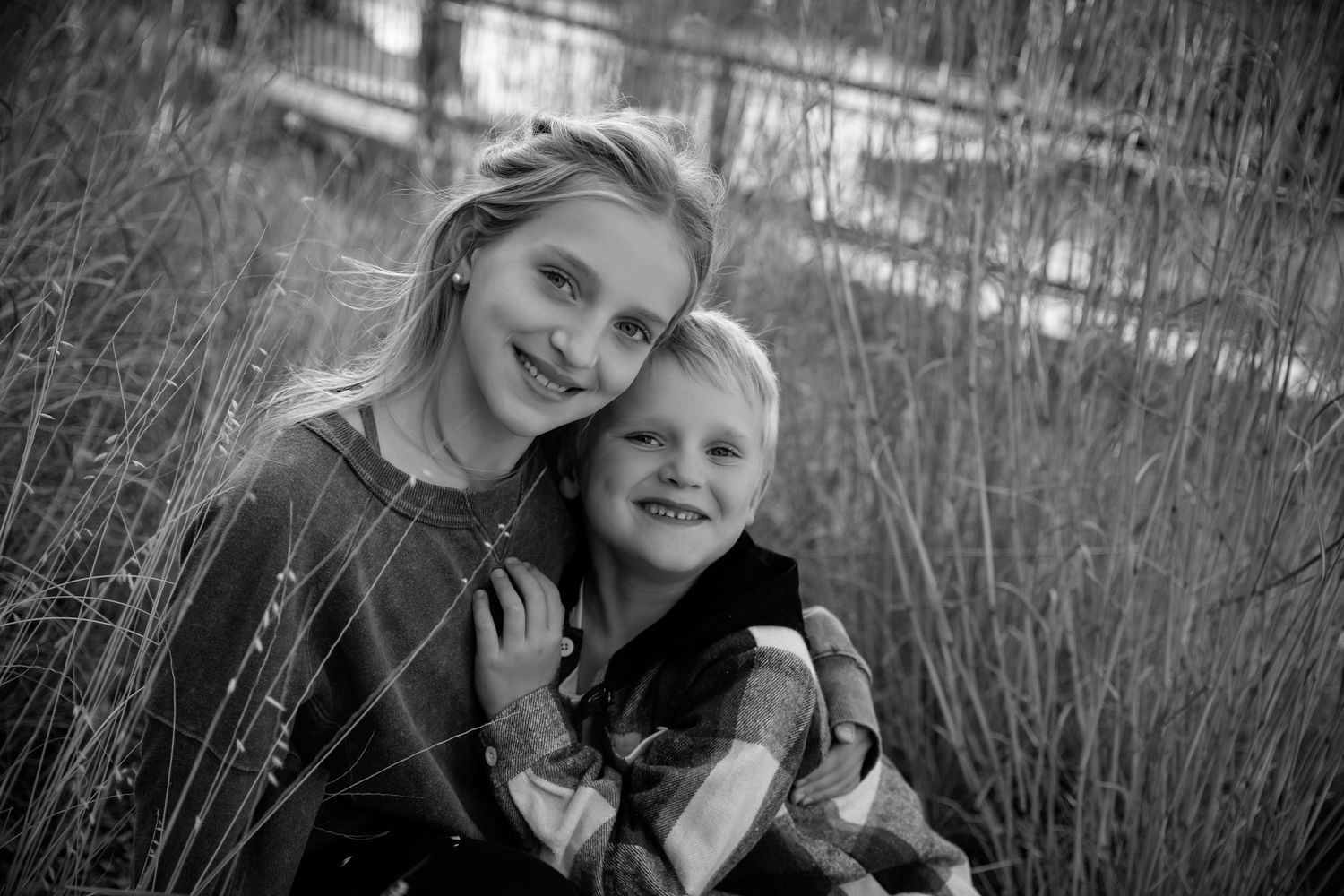 Black and white portrait of two children sitting together outdoors among tall grasses.