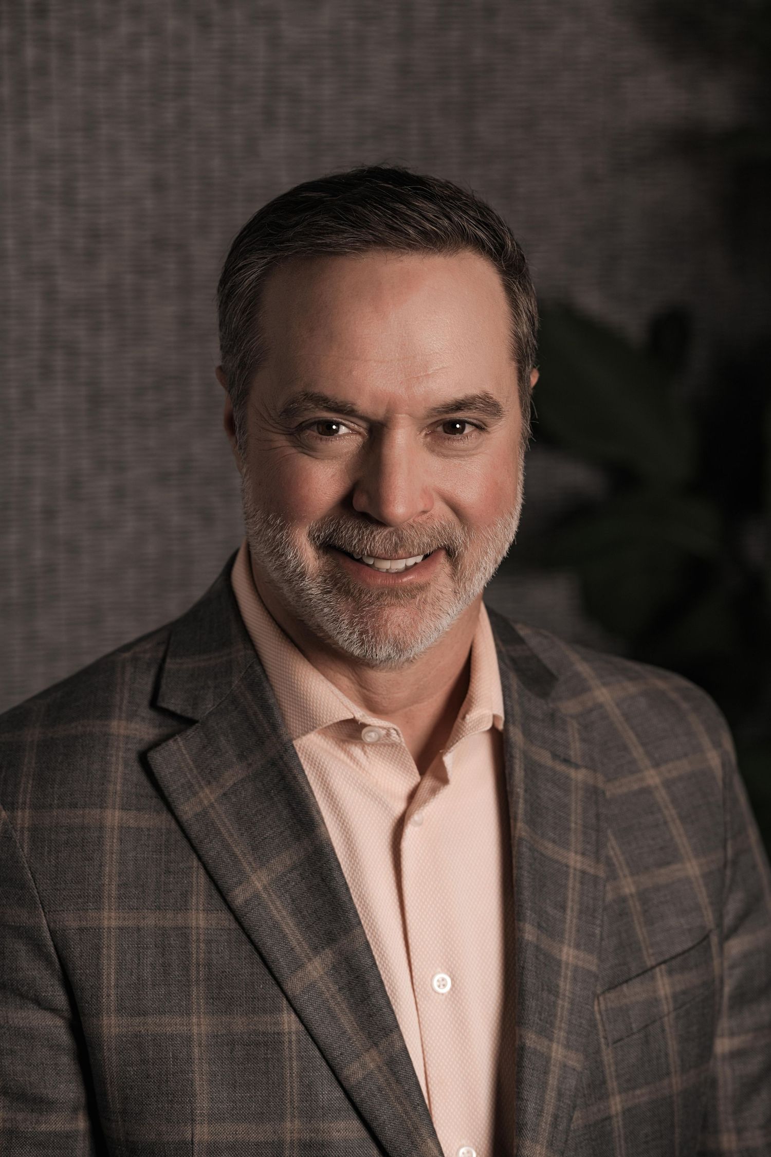 Professional headshot series showing a person in a plaid blazer and light colored shirt against a dark background.