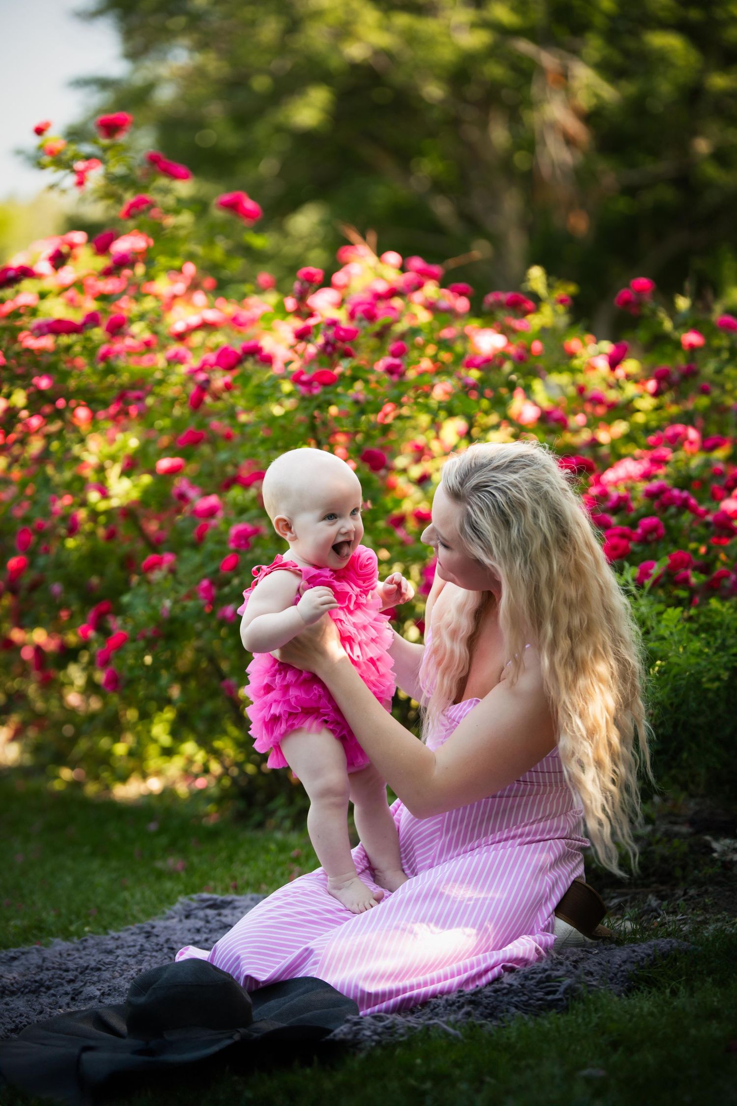 Loving moment captured on blanket surrounded by blooming pink flowers in garden.