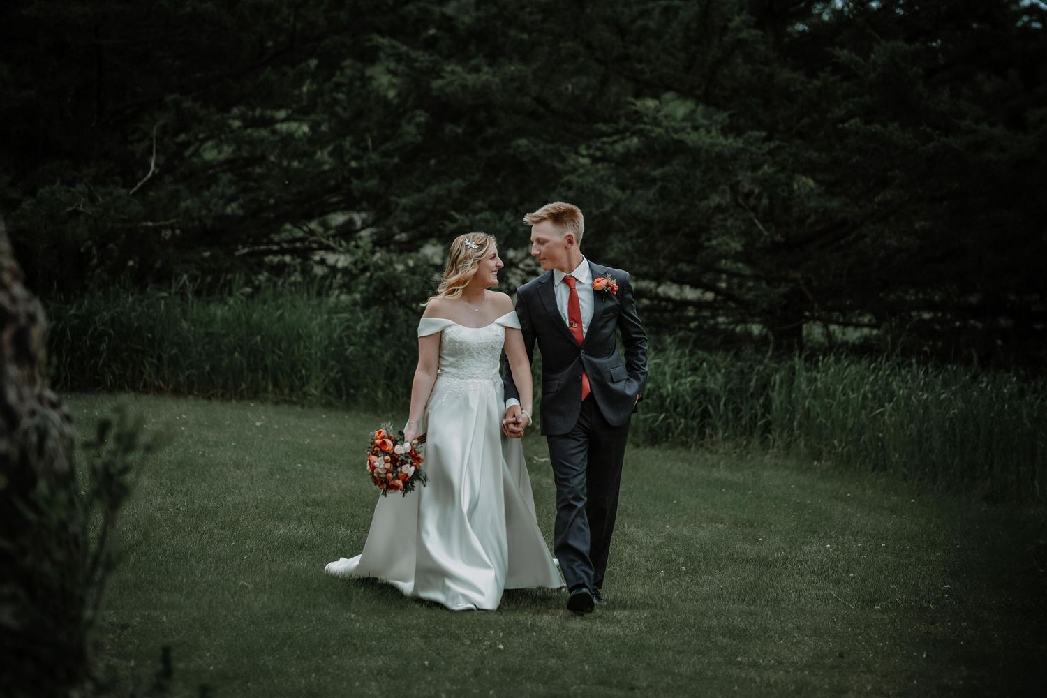 Romantic couple walking together through a grassy meadow on their wedding day.