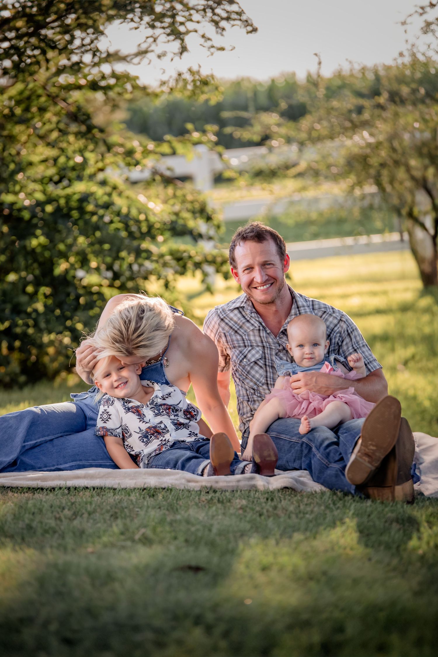 Family sharing playful moment together on blanket during sunset.