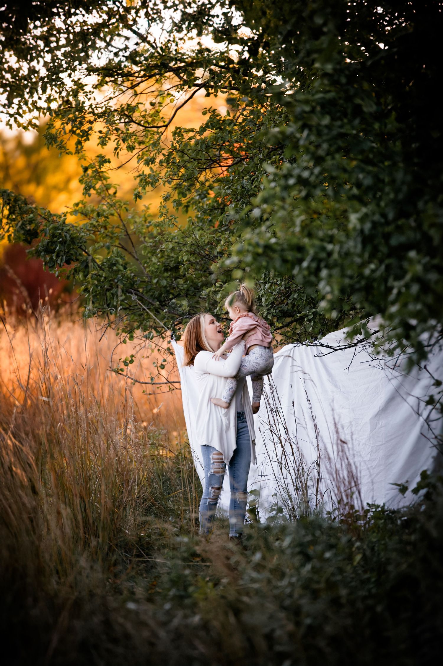 Family spends time together during golden hour in a field with tall grass and trees at sunset.