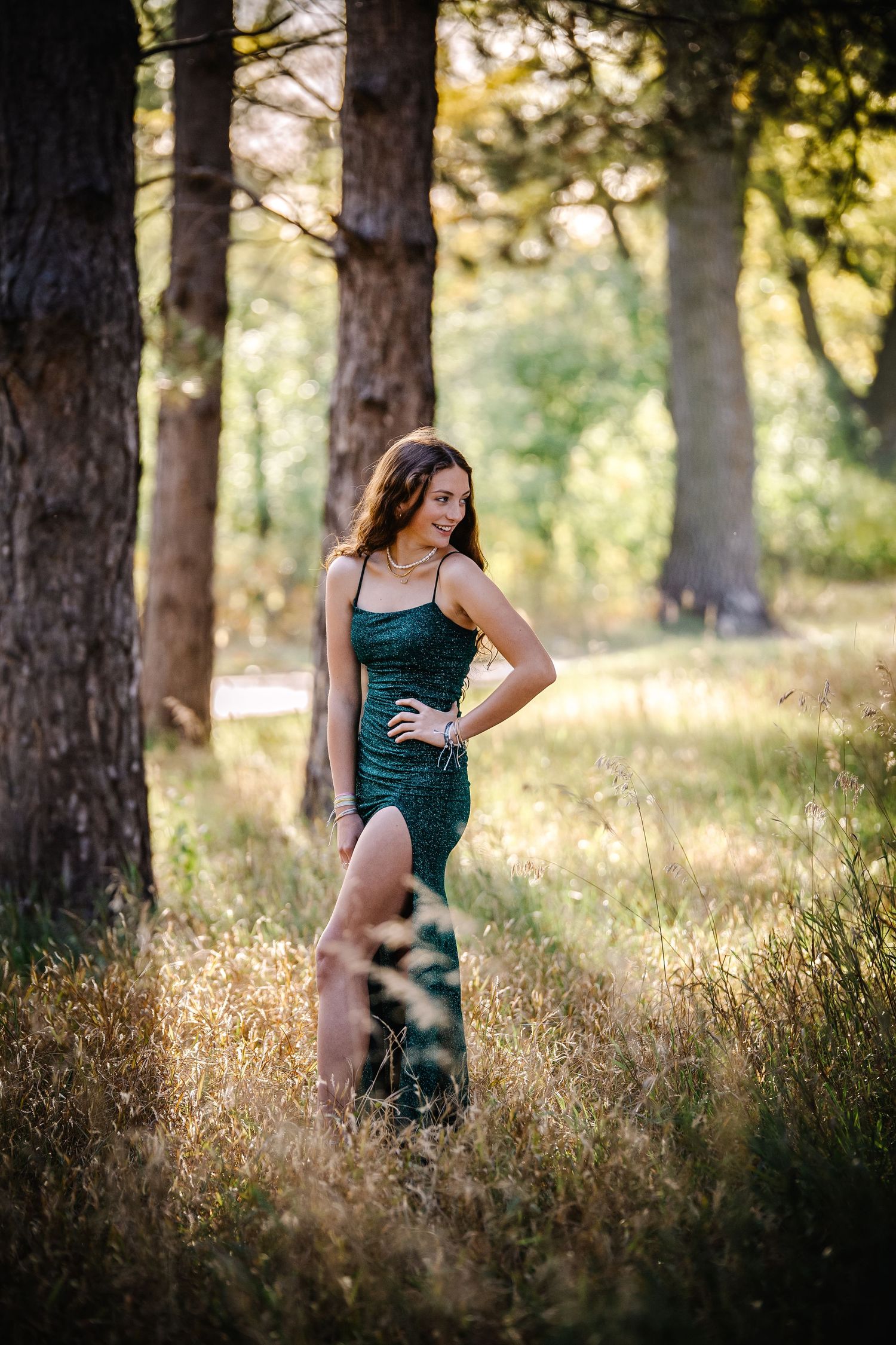 Woman in elegant green dress poses in dreamy forest setting with golden sunlight. Photographer in Sioux Falls, SD