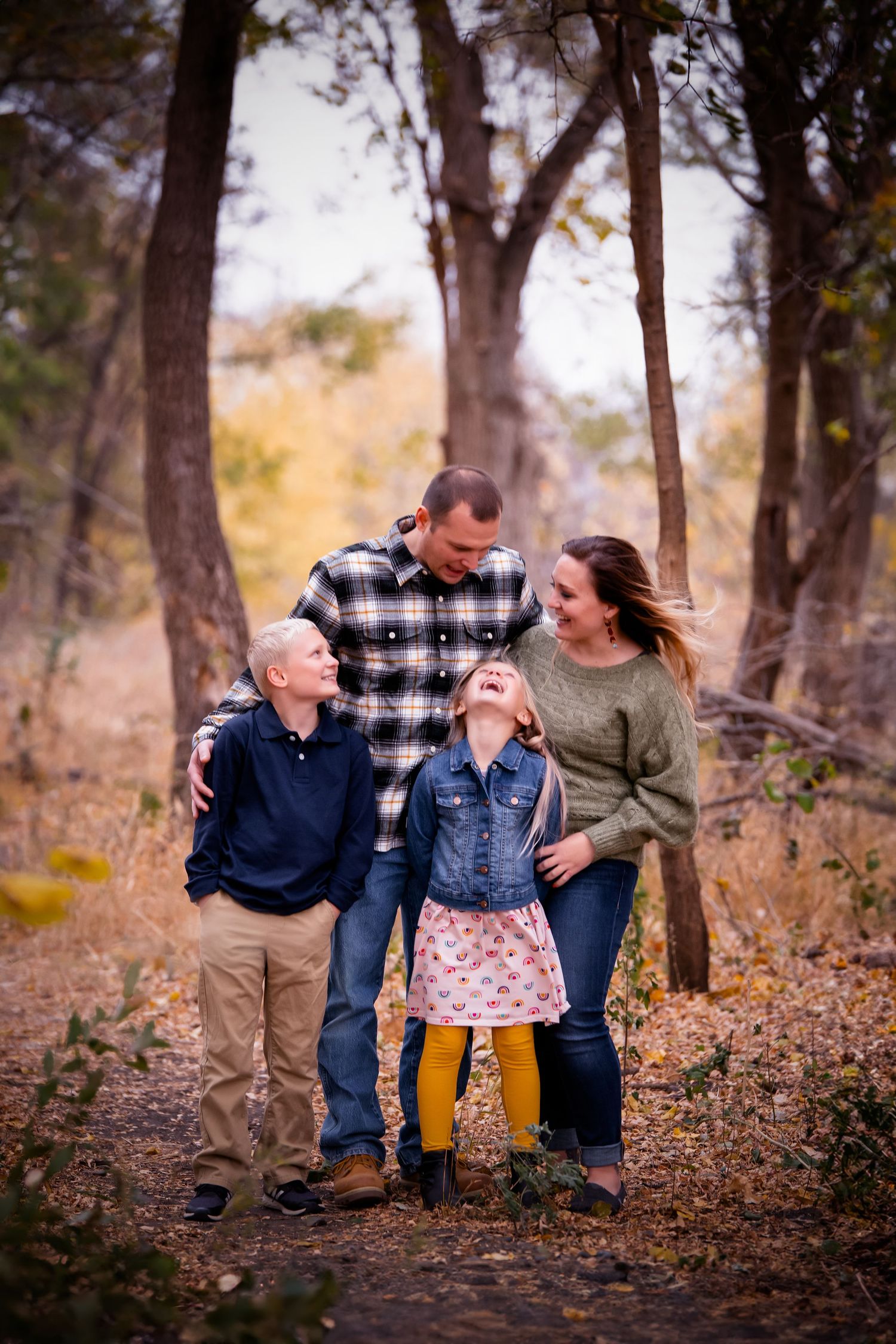 A family of four walking together and laughing on a forest trail during autumn.