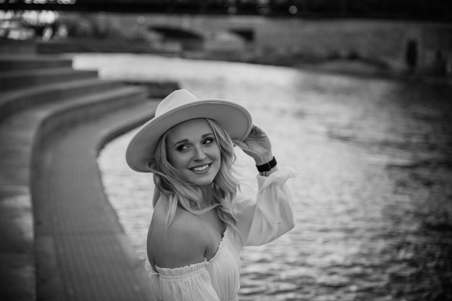 Black and white portrait of someone in a hat near water at sunset creating a dramatic silhouette effect.