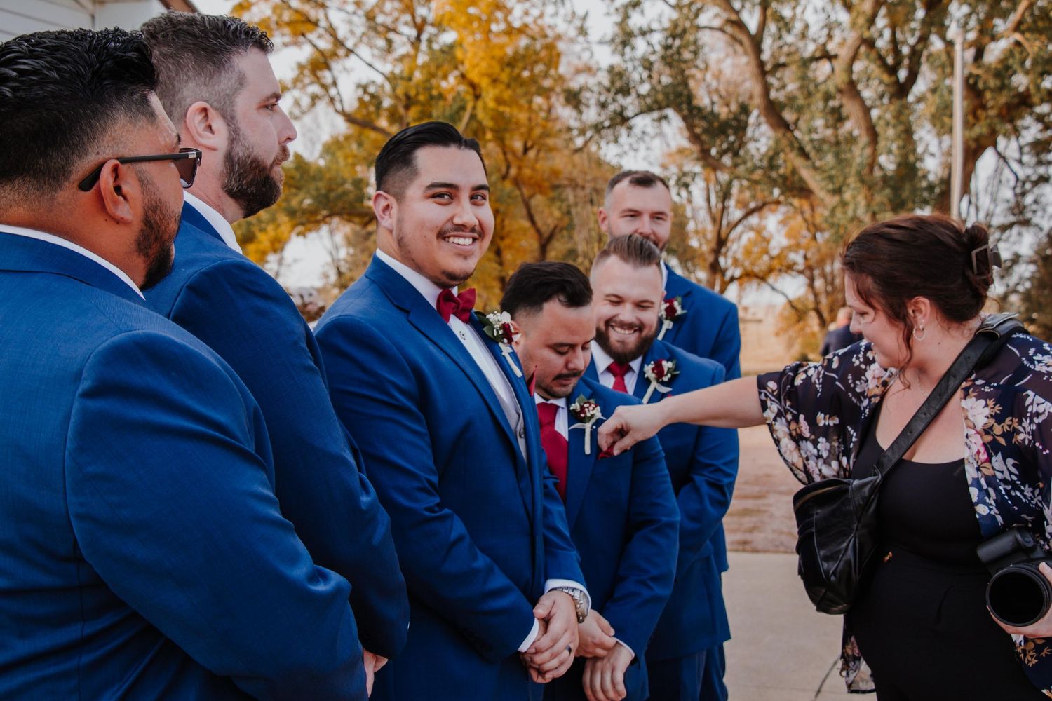 Wedding party in navy suits shares laughs outdoors during autumn celebration.