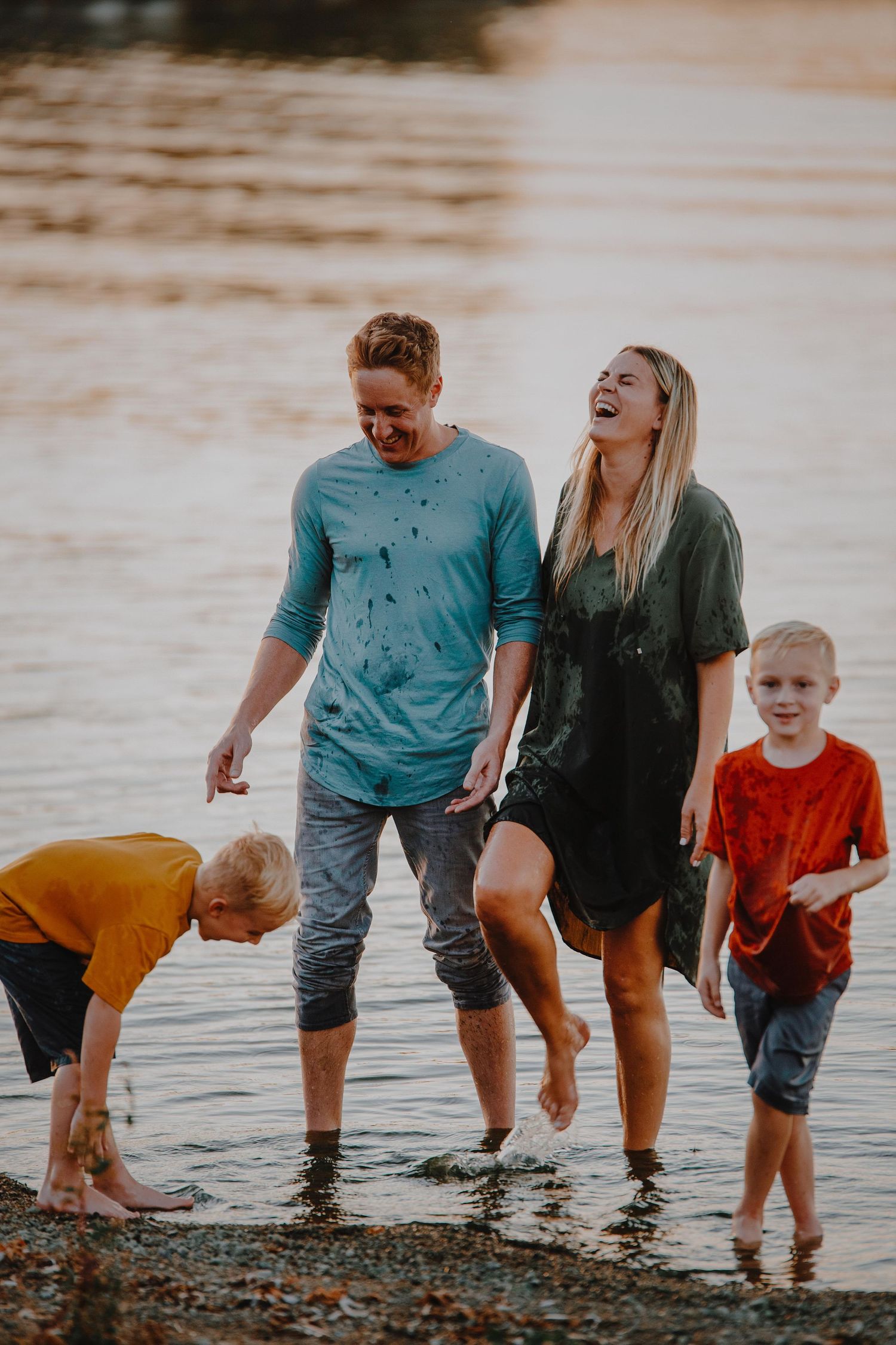 Family enjoying a sunset walk along the shoreline, splashing in shallow water together.