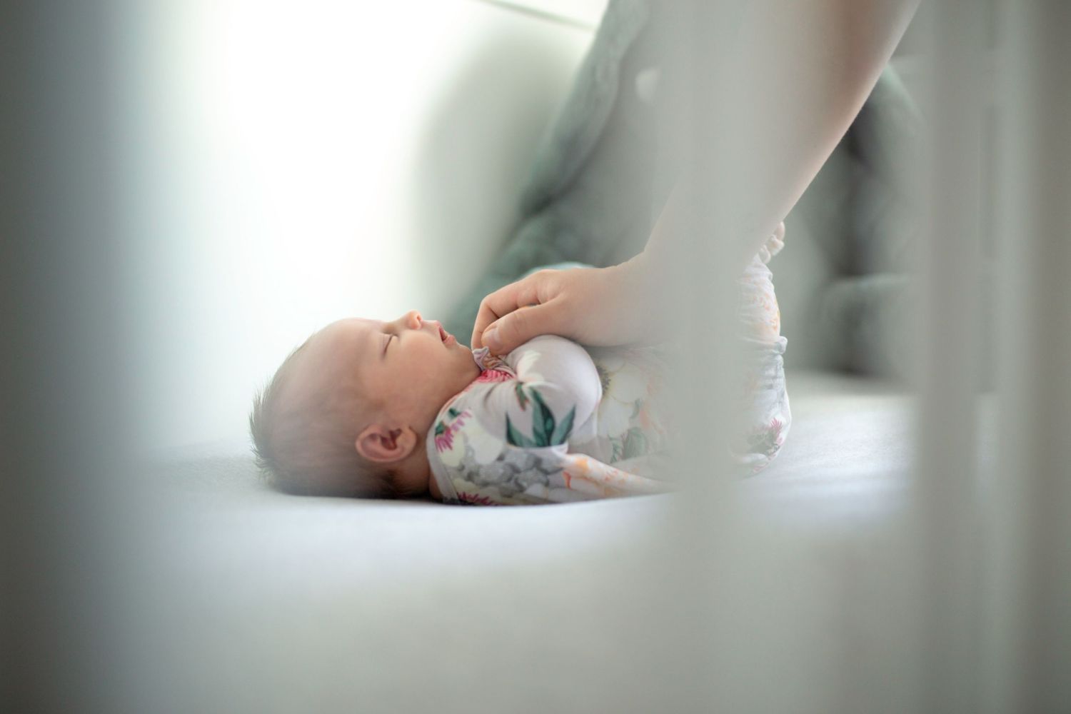 View through crib slats of sleeping baby in light-filled nursery.