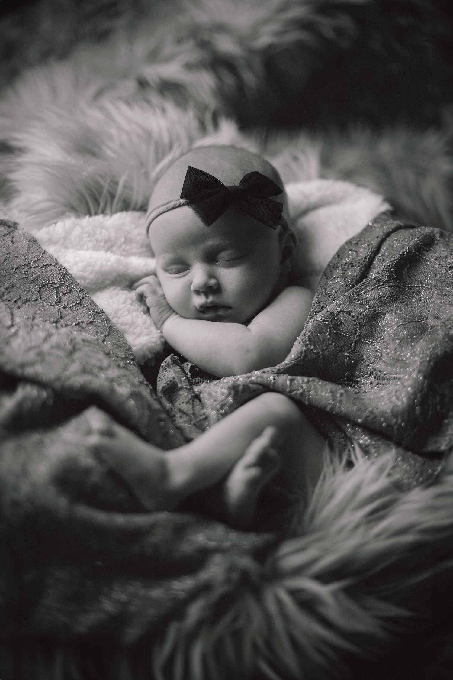 Black and white portrait of sleeping baby wearing bow headband on textured blanket. Photographer in Sioux Falls, SD