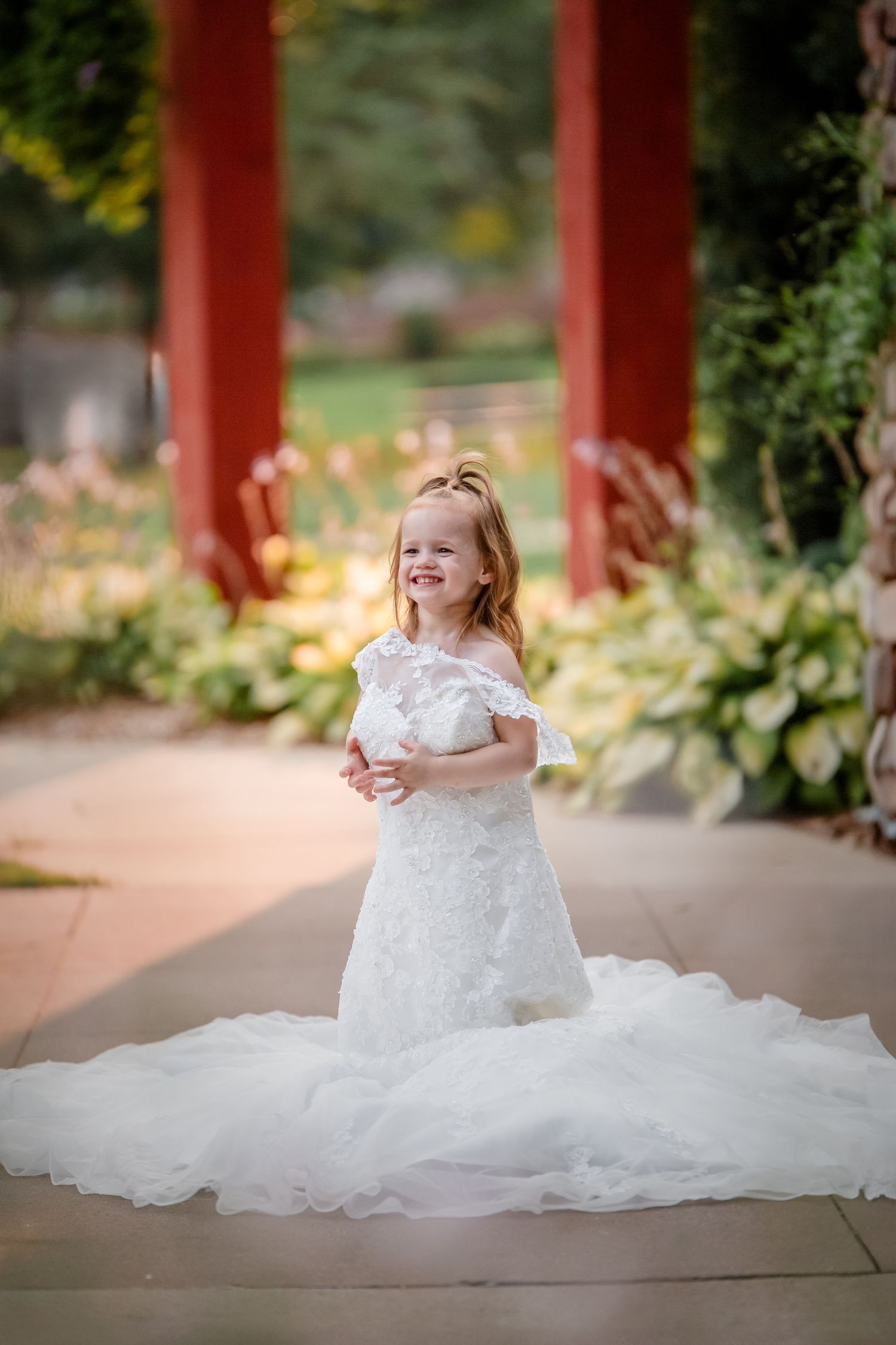 A delightful scene of a child wearing a flowing white dress sitting and playing on a covered outdoor patio.