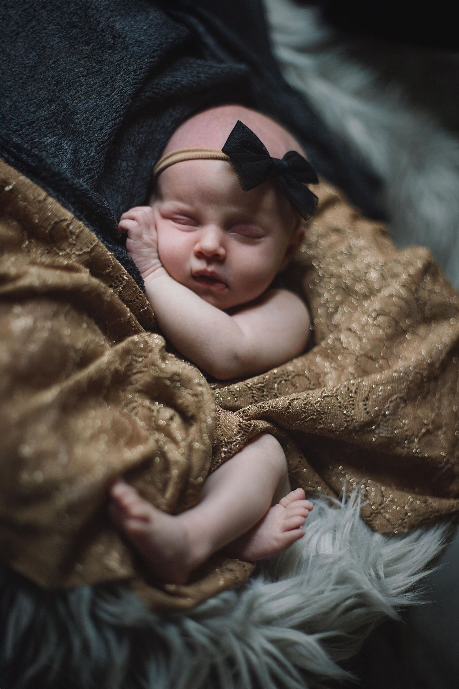 Close-up of sleeping baby with black hat nestled in brown blanket and grey fur.