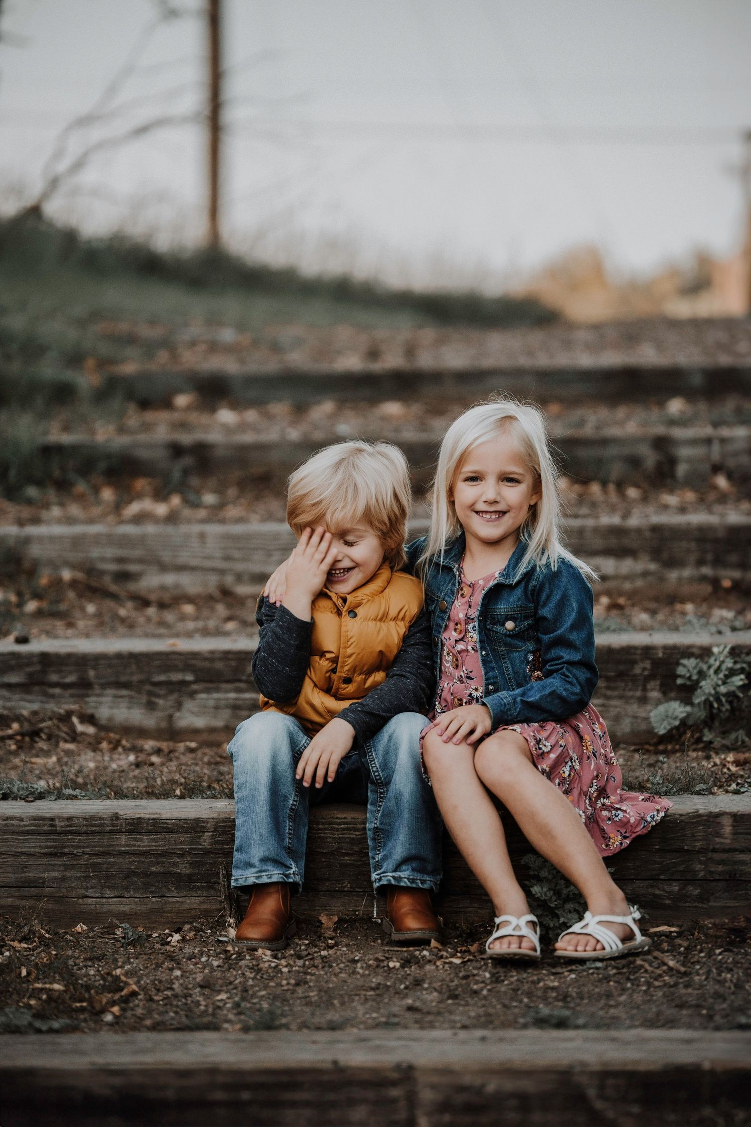 Siblings sitting together on wooden steps during an outdoor photo session.