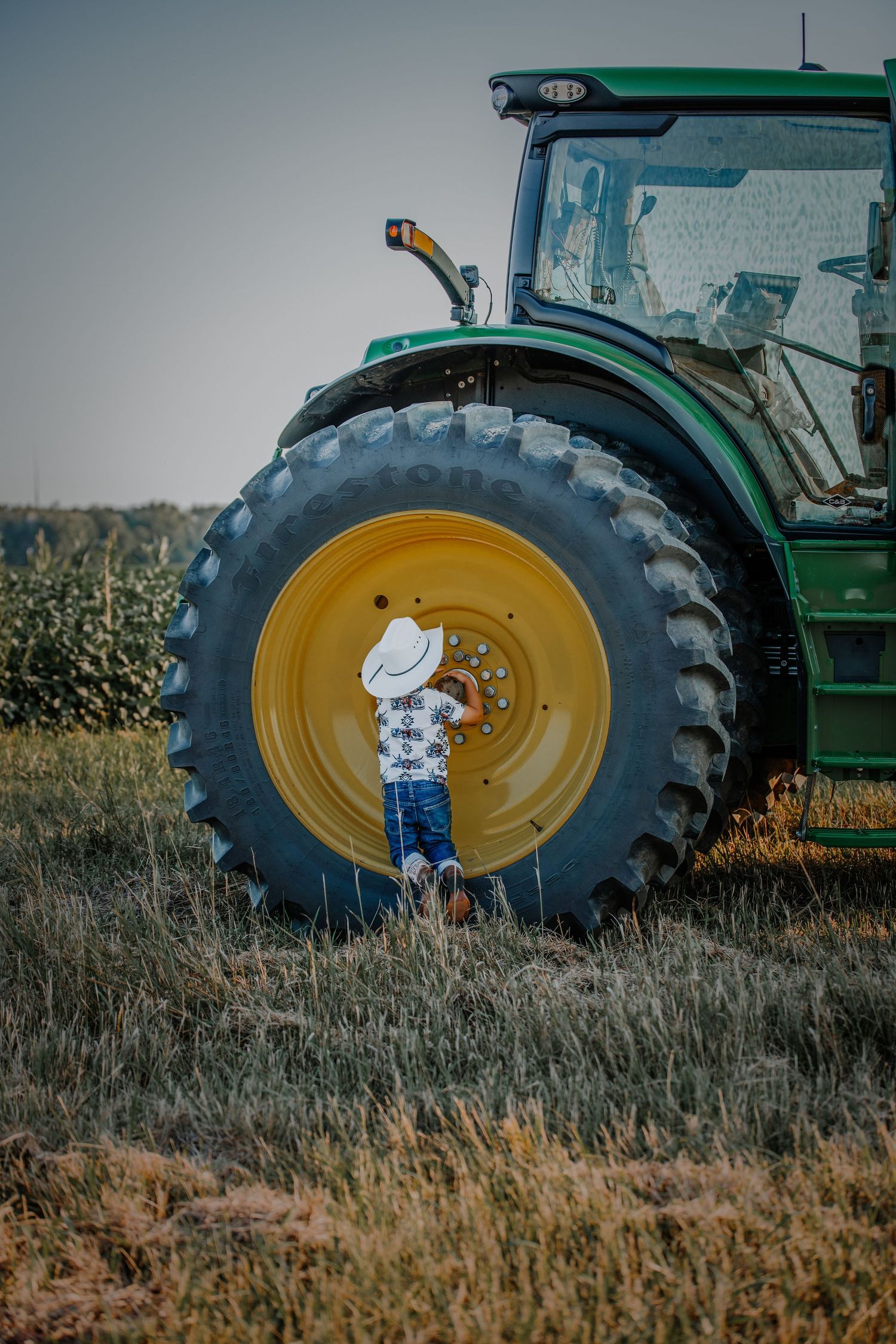 Child poses next to massive tractor tire in agricultural setting.