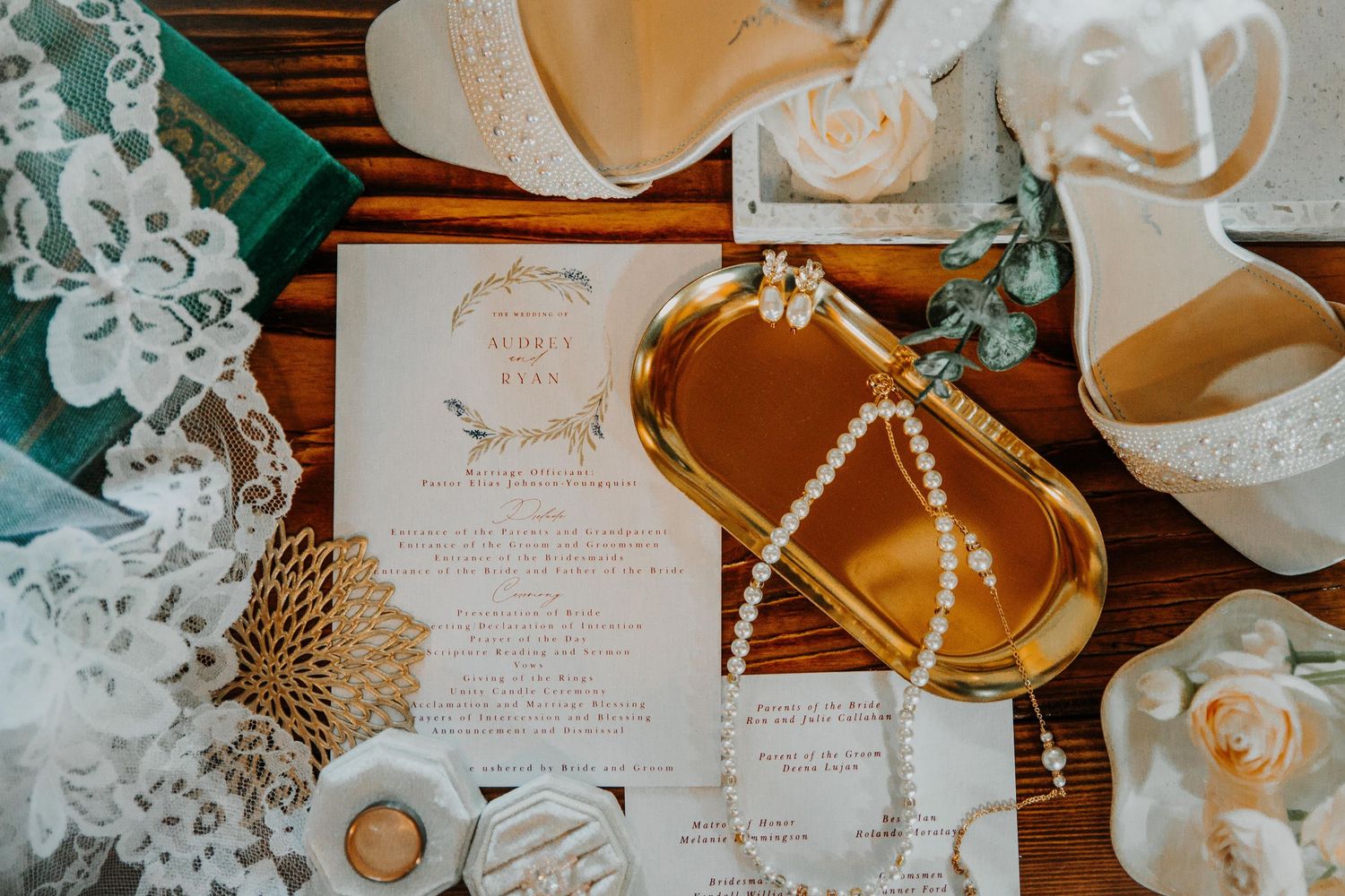 Wedding details flatlay with invitation, pearls, and delicate floral accents on gold tray.
