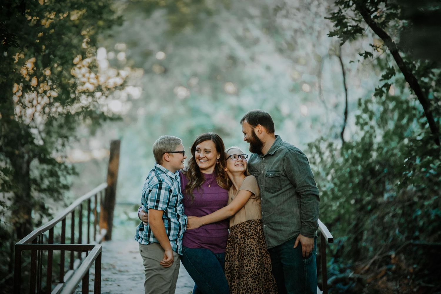 Family members share intimate moments during outdoor photography session under trees.