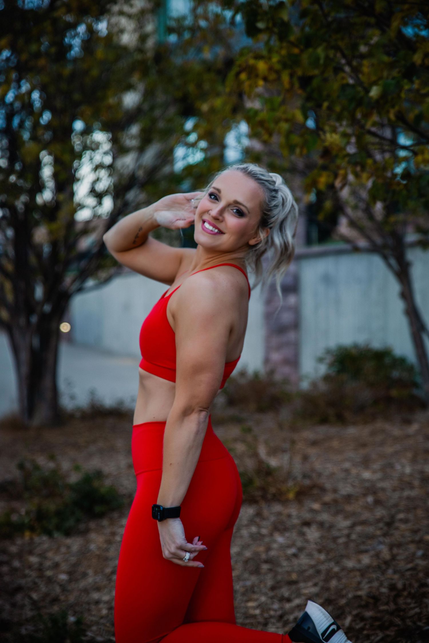 A woman in a fitted red dress poses playfully outdoors against a natural backdrop.
