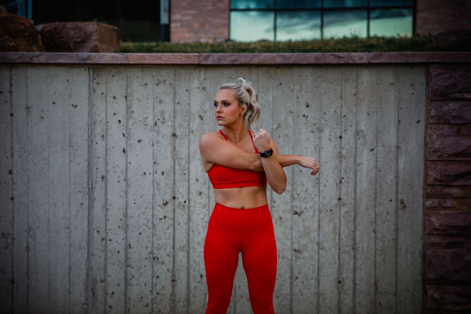 Athlete in red workout attire performs dynamic exercises against concrete wall background.