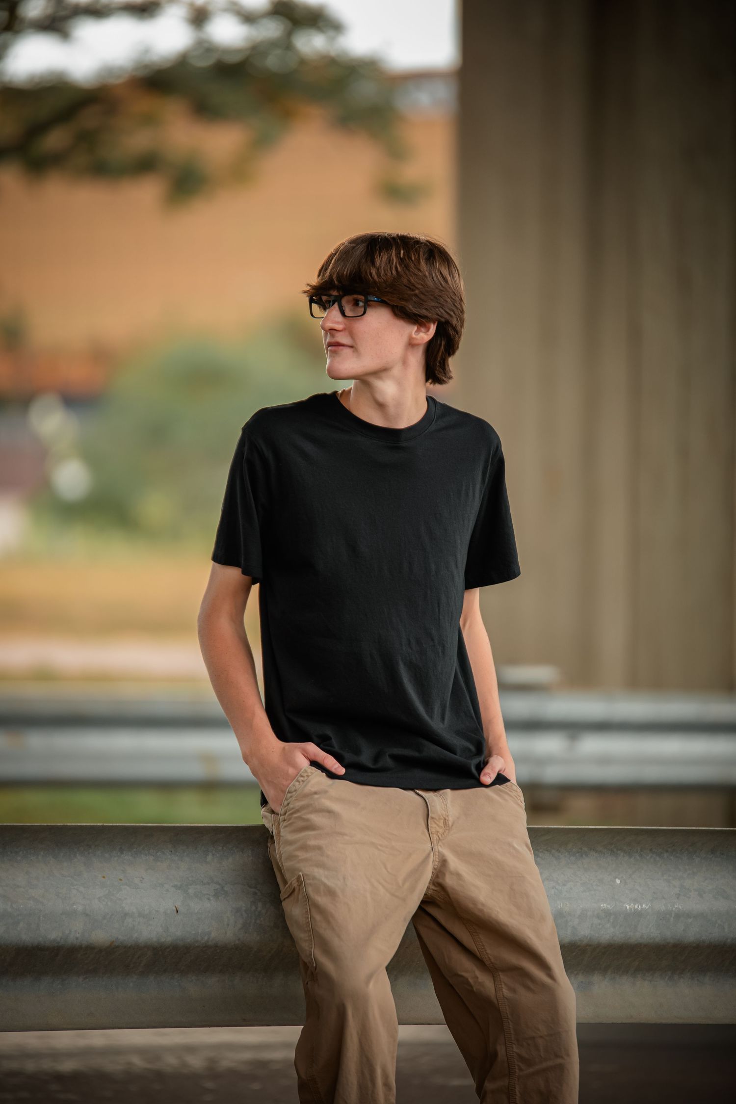 Person in black t-shirt and khaki pants leaning against concrete wall. Photographer in Sioux Falls, SD