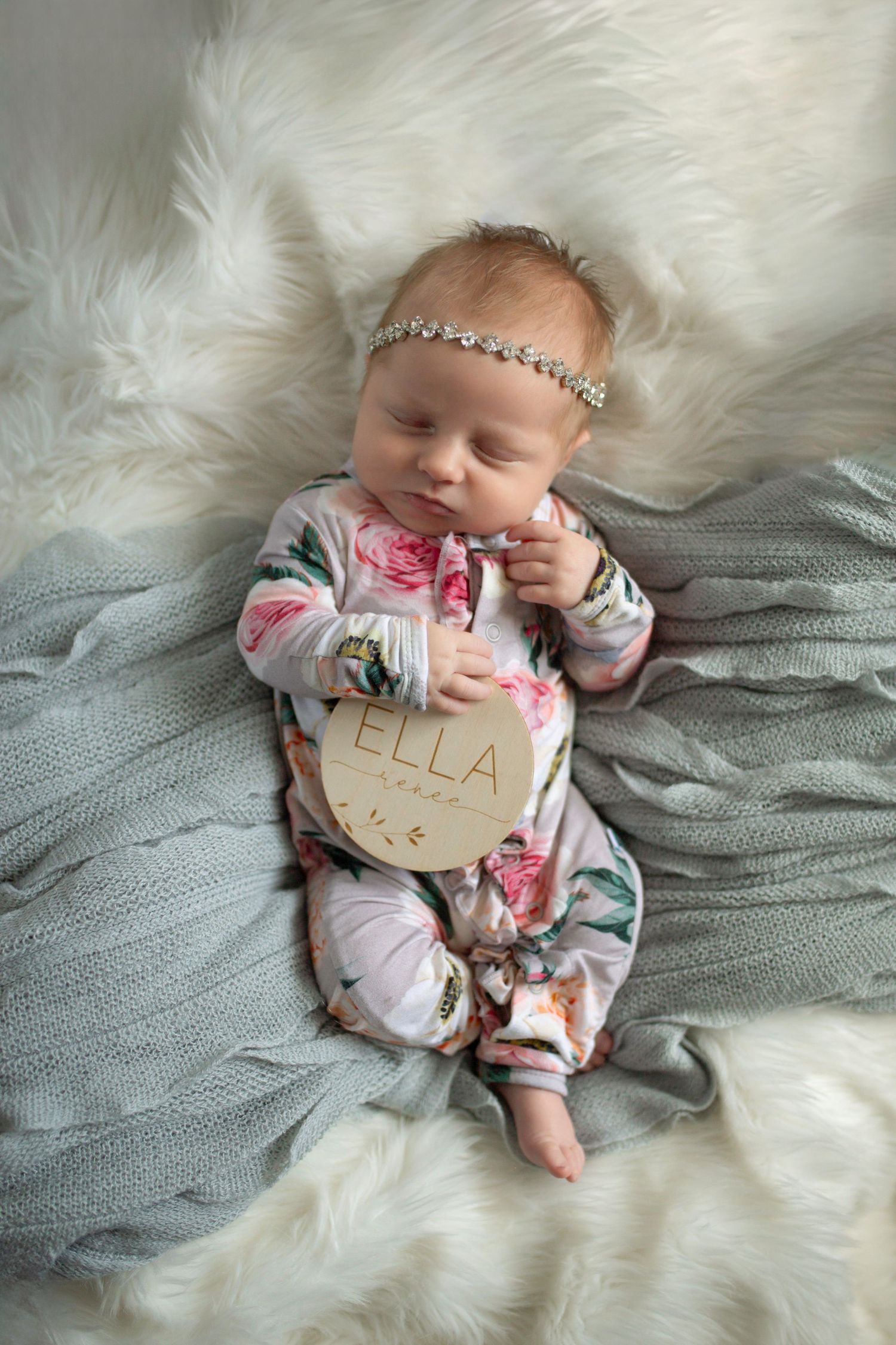 Newborn rests on white fur with gray blanket and sparkly headband.
