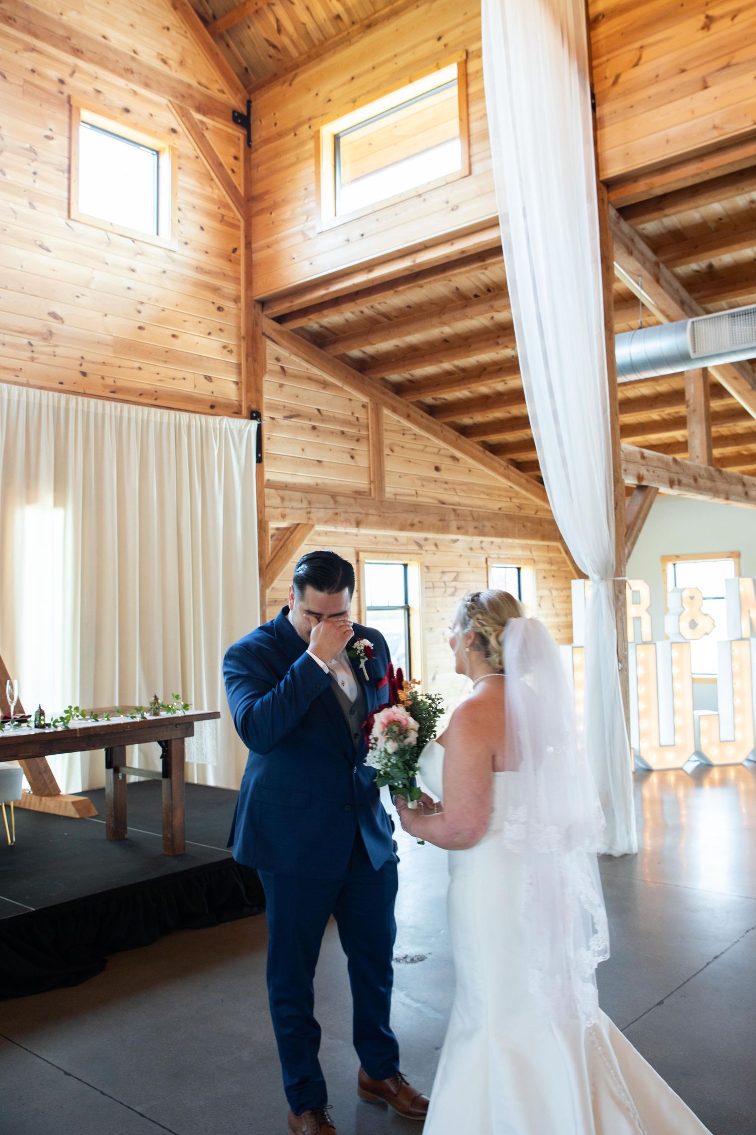 A couple sharing a beautiful first look moment in a rustic wooden venue with natural lighting.