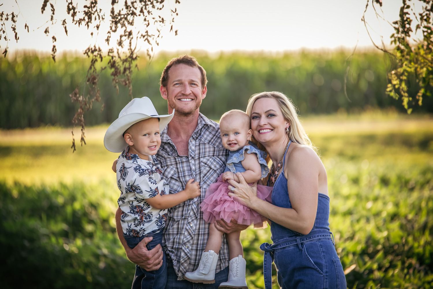 A group poses together in a sunlit field at golden hour with trees and natural foliage in the background.