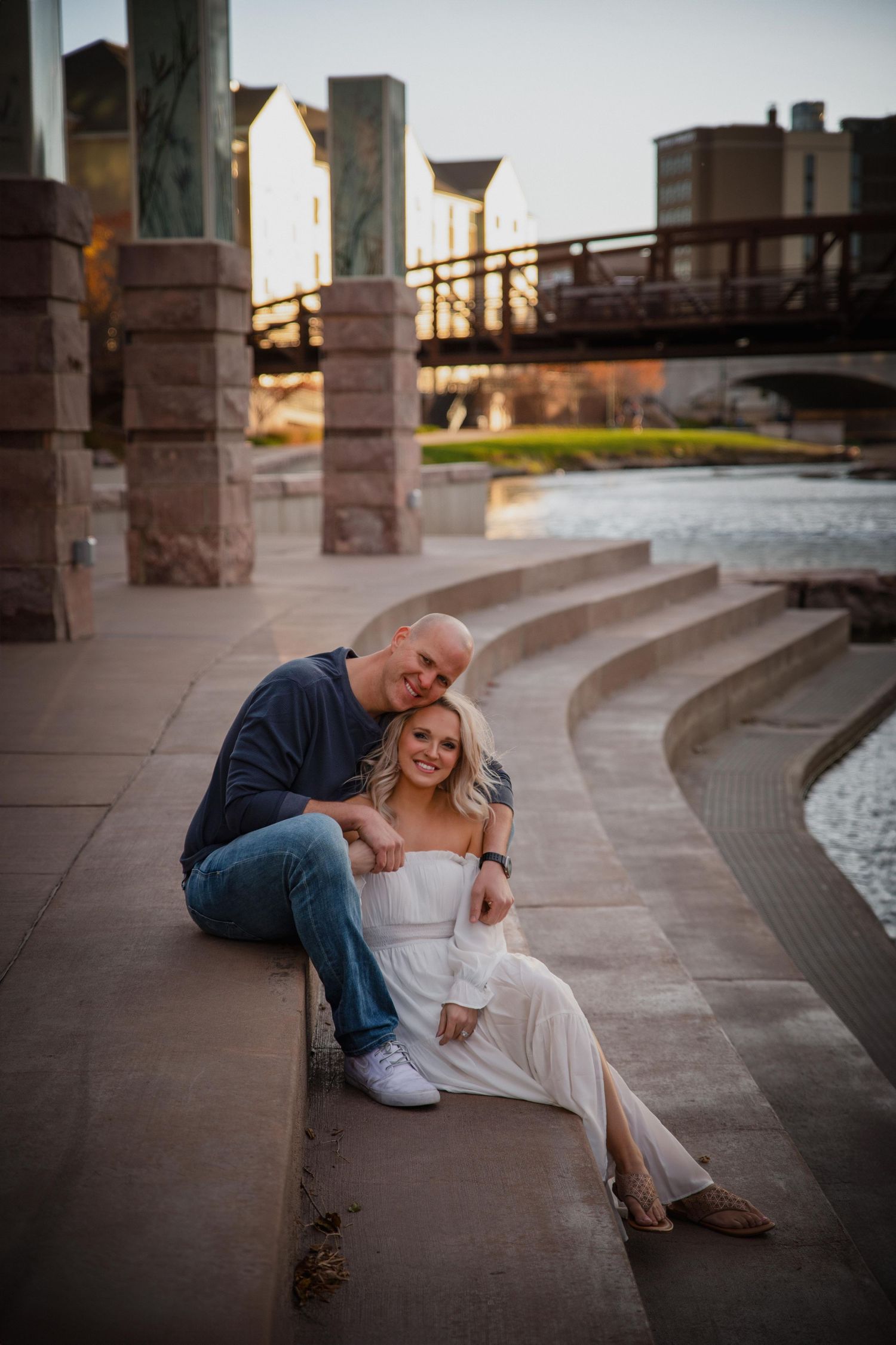 A couple sits together on curved stone steps at dusk with architectural columns in the background.