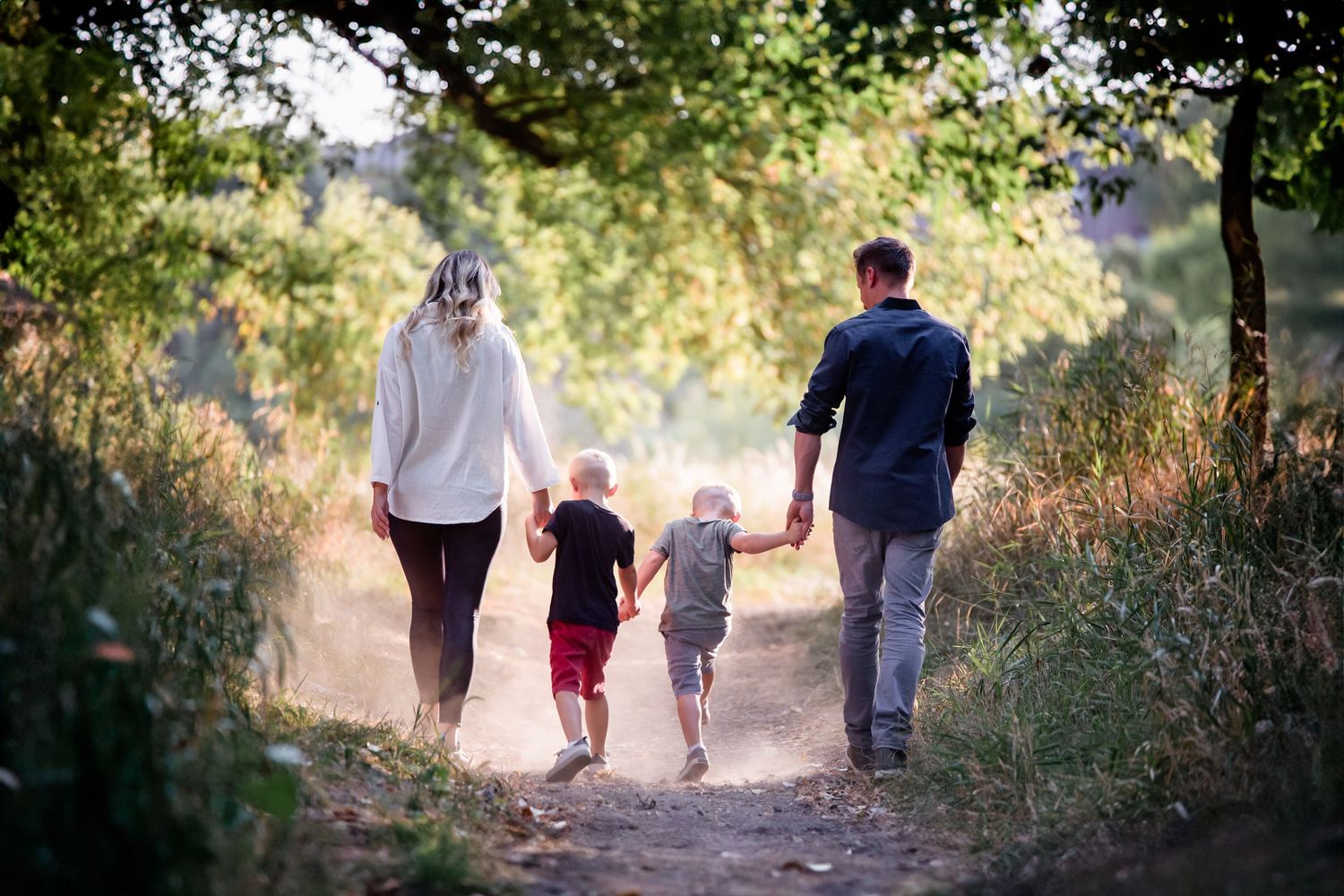 A family walks together on a nature trail with sunlit foliage visible in the background.