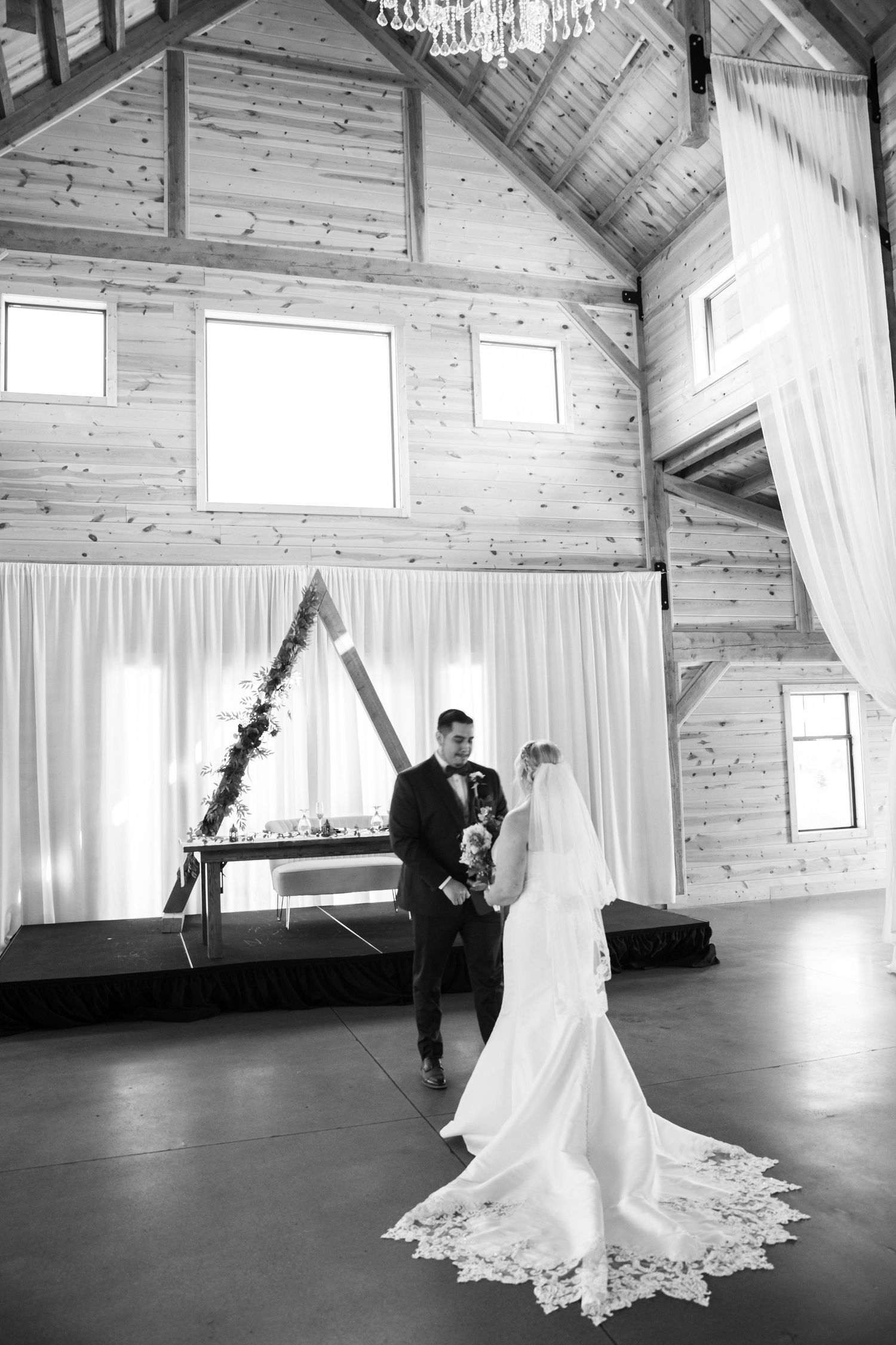 First look moment captured in a rustic wooden barn venue with white curtains.
