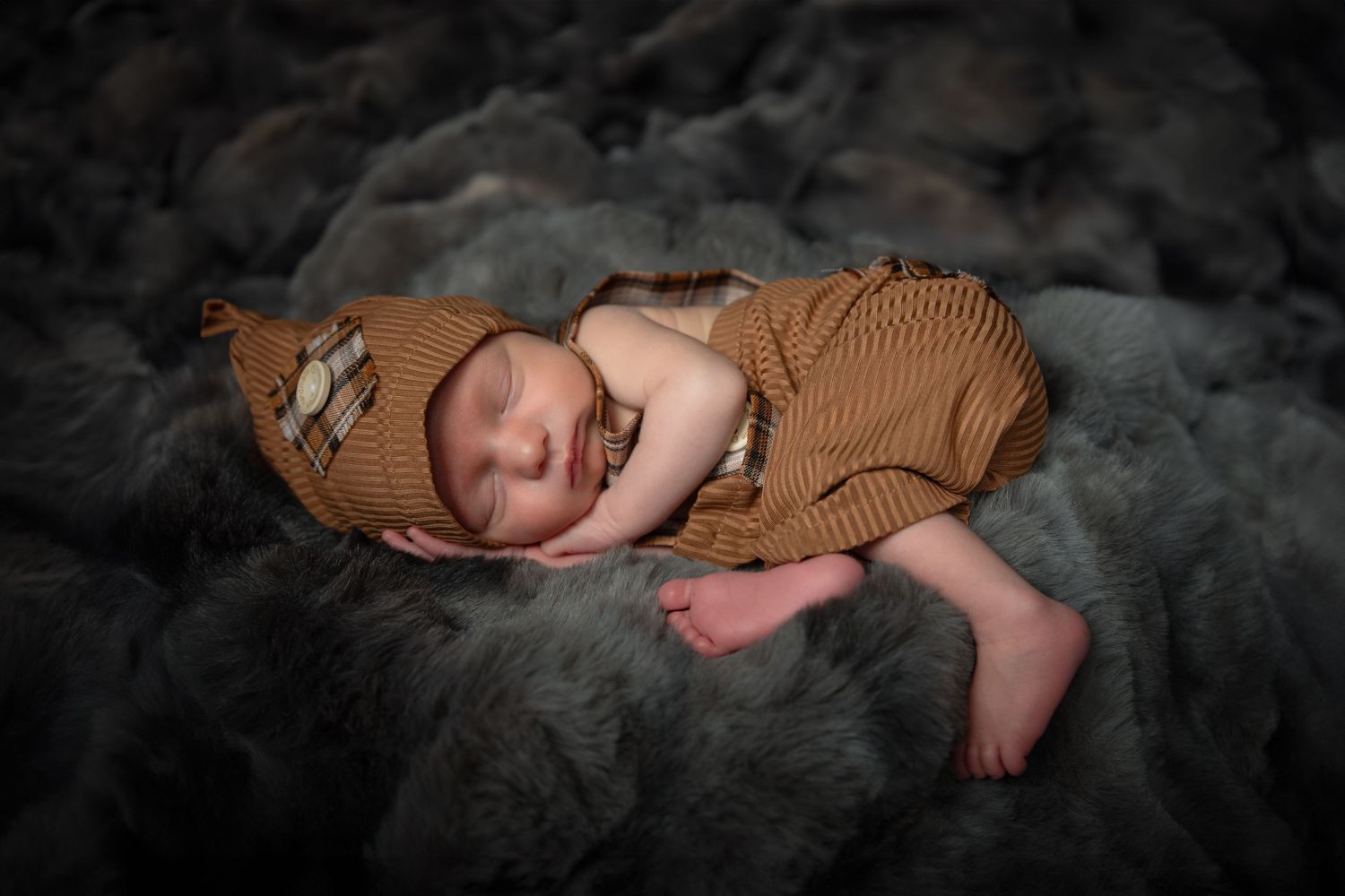 Baby wearing brown knit sweater sleeping peacefully on soft gray blanket.