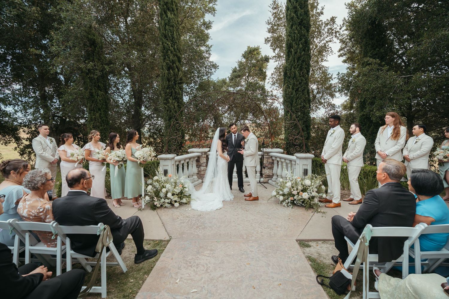 Outdoor wedding ceremony setup with white chairs arranged in rows along a tree-lined path at sunset.