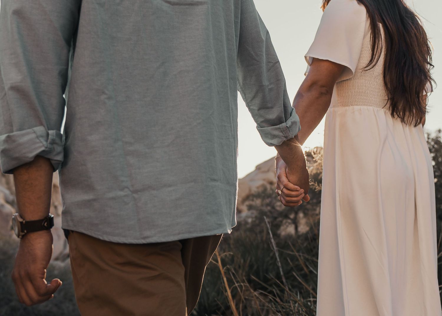 A couple holding hands while walking in a desert landscape at sunset.
