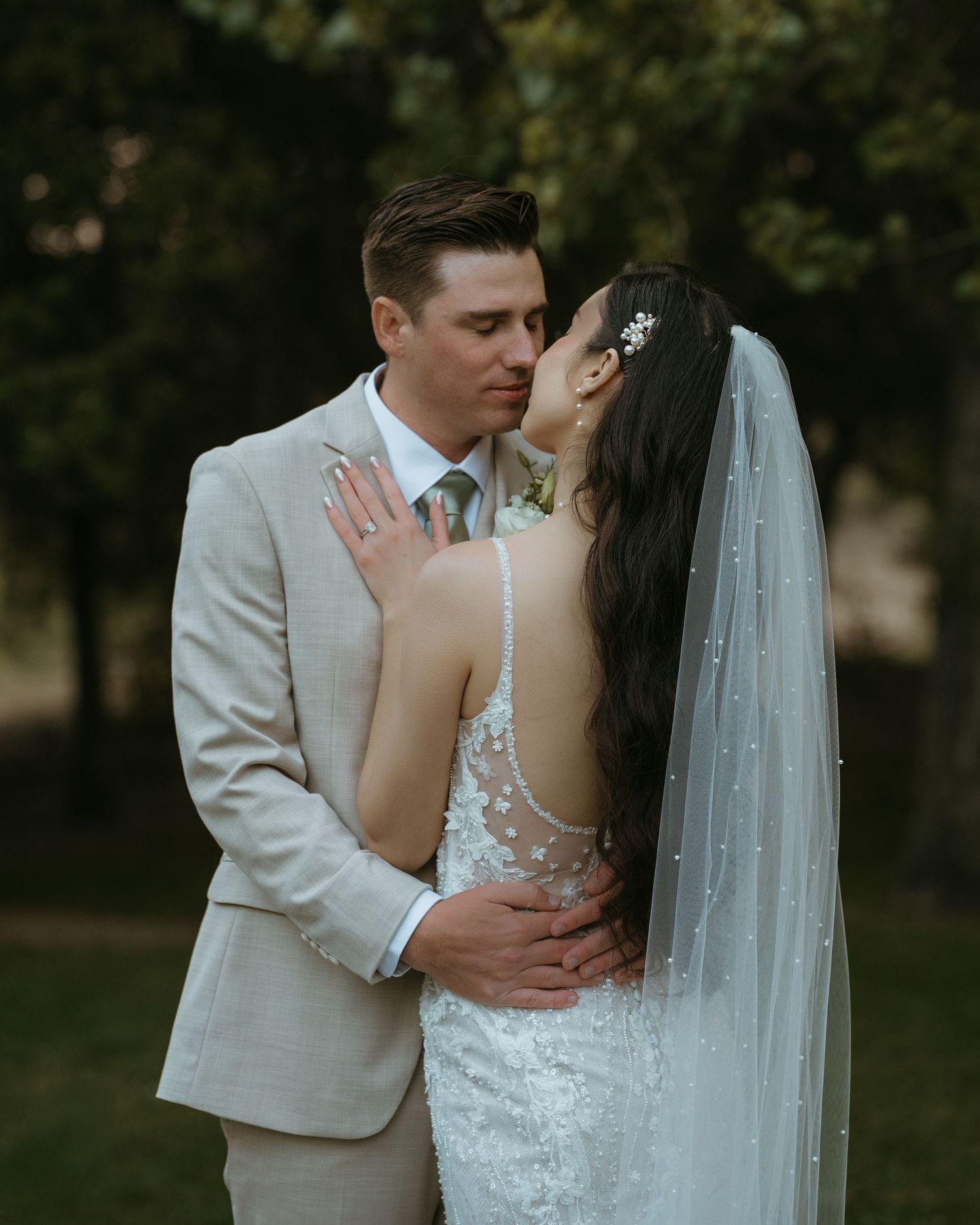 Romantic wedding couple embraces outdoors in a garden setting with soft lighting and flowing white veil.