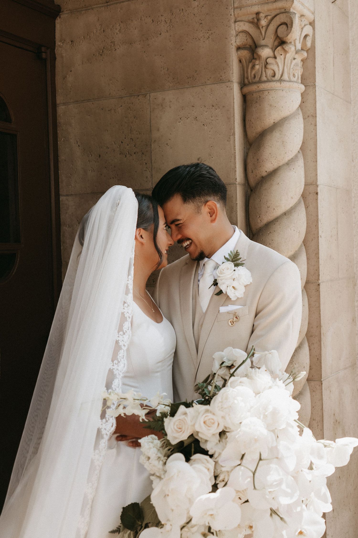 Romantic wedding couple embraces in elegant church setting with white floral bouquet and flowing veil.