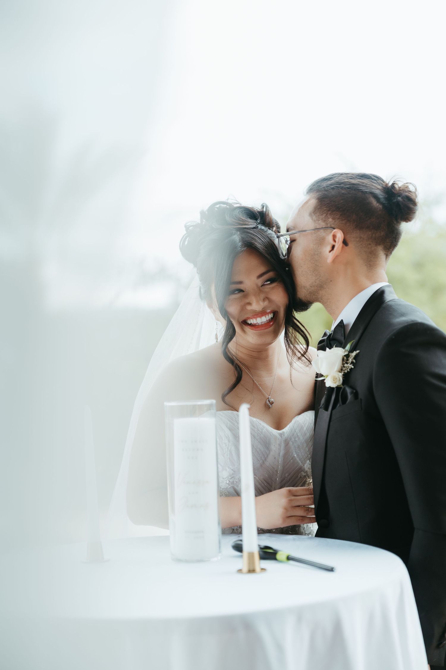 A romantic moment between newlyweds sharing laughter and tender moments at their wedding reception table.