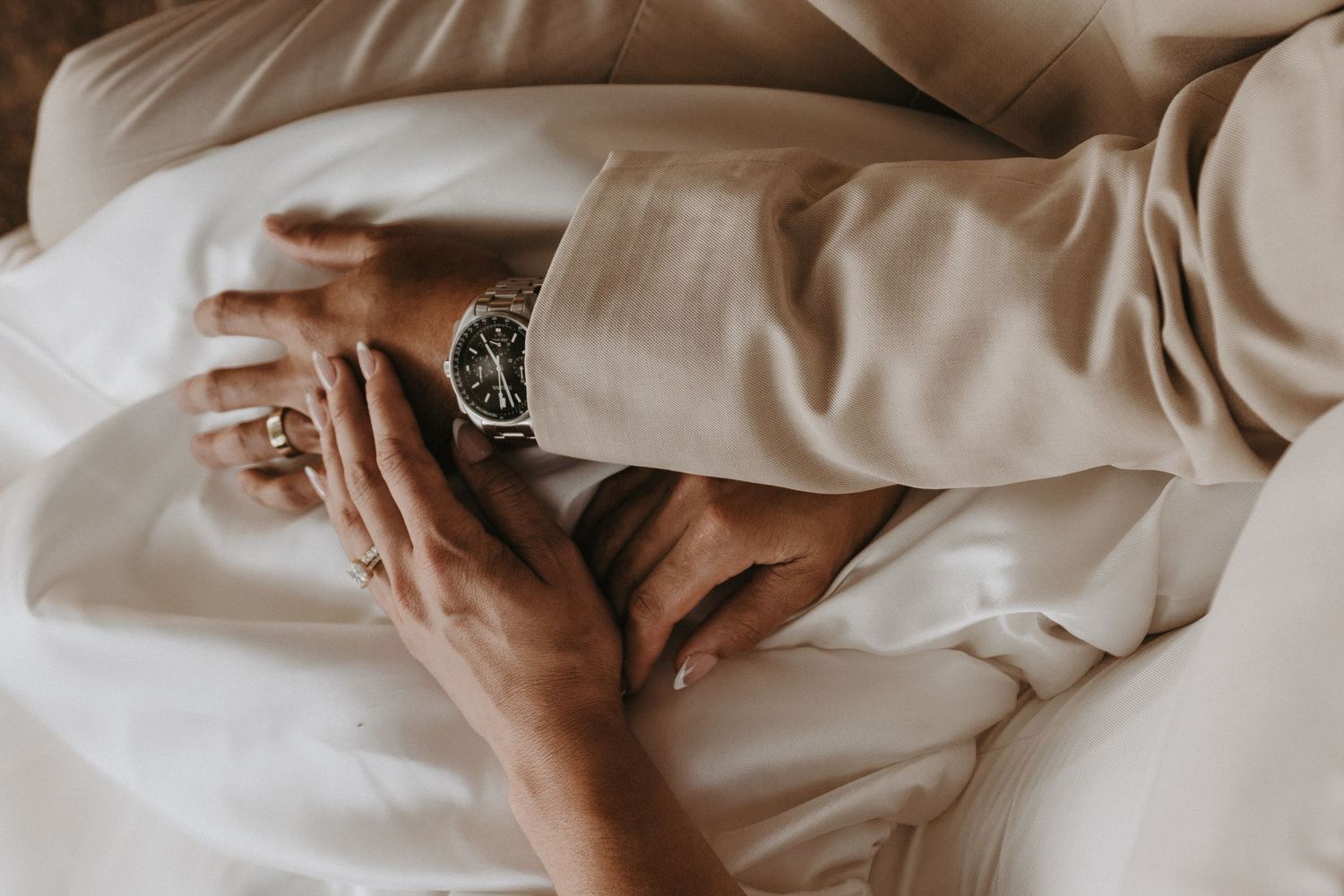 Two hands gently touch white bedsheets in soft morning light creating an intimate and peaceful atmosphere.